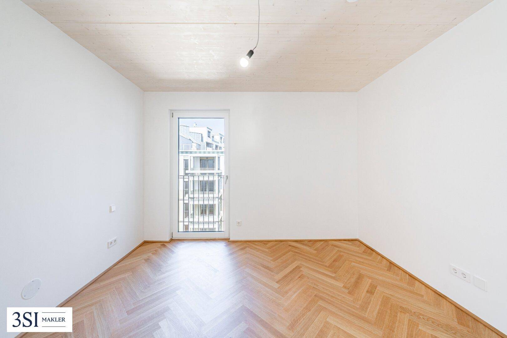 Helles Schlafzimmer mit Fischgrätparkett und Zugang zu einem französischen Balkon.