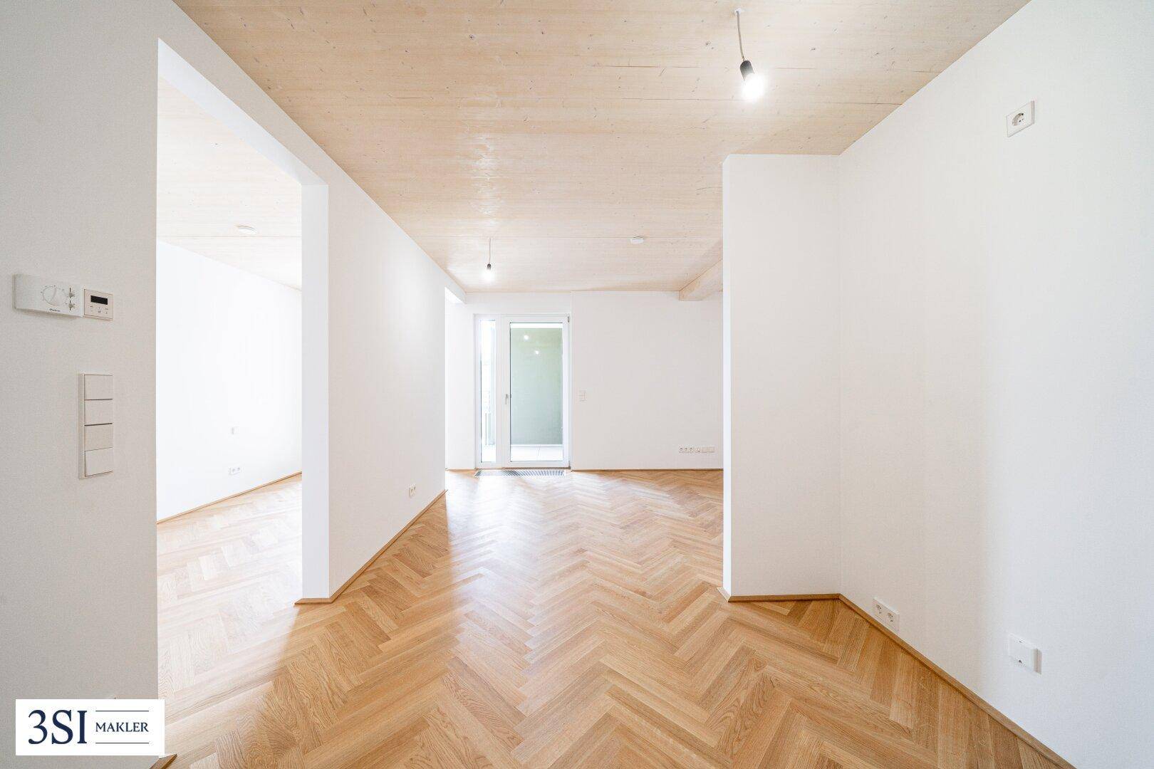 Helles, offenes Zimmer mit Fischgrätparkett und Zugang zu einem Außenbereich.