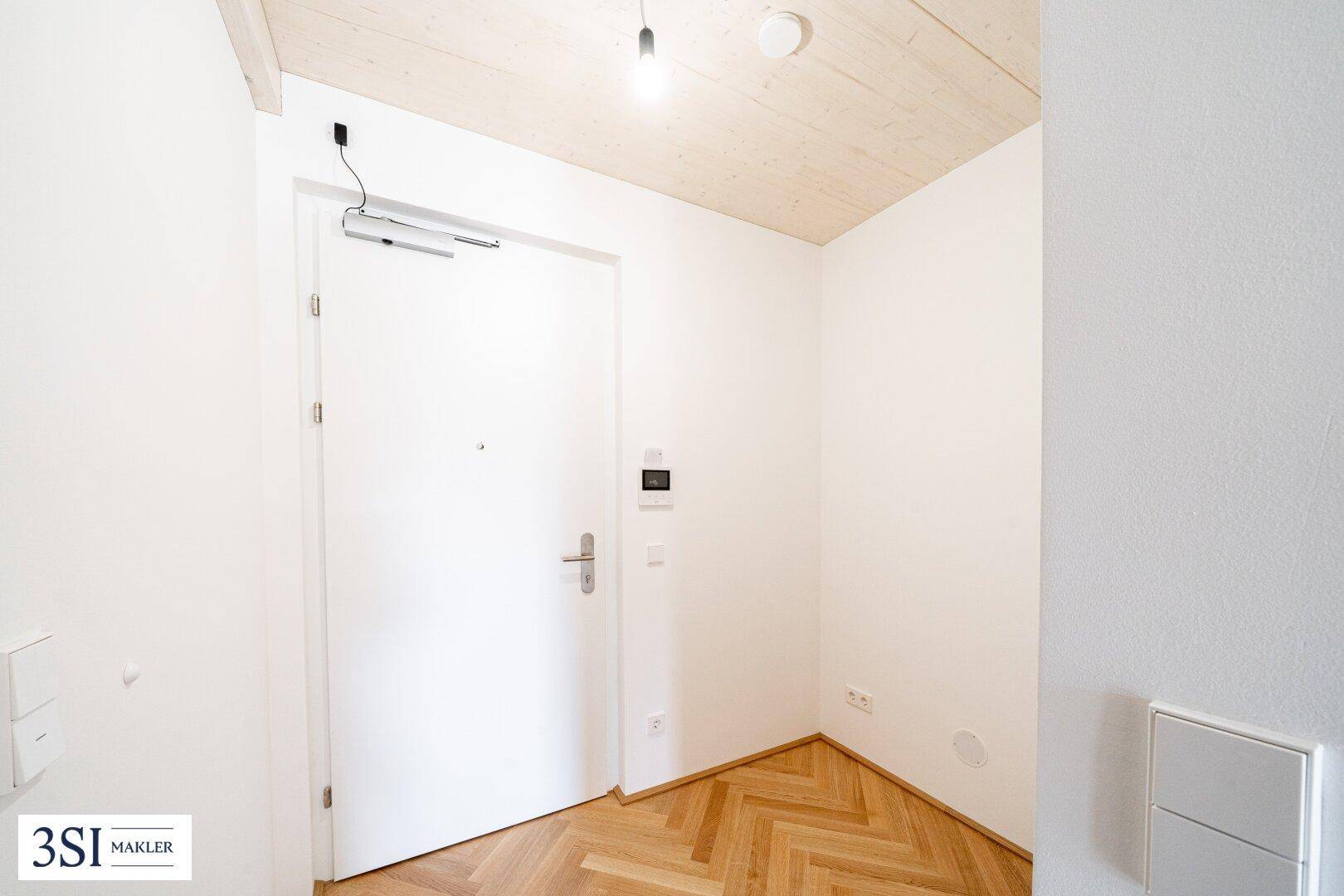 Eingangsbereich mit heller Holztür, Fischgrätparkett und moderner Holzdecke.