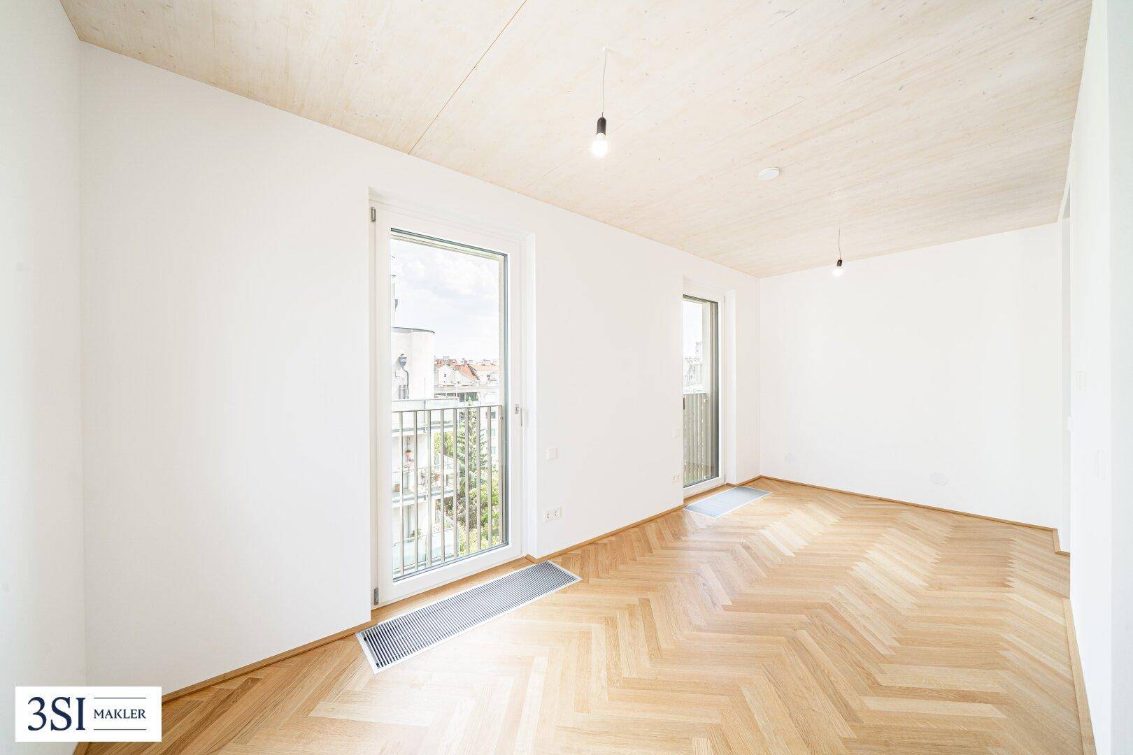 Helles Zimmer mit zwei französischen Balkonen, Fischgrätparkett und moderner Holzdecke.