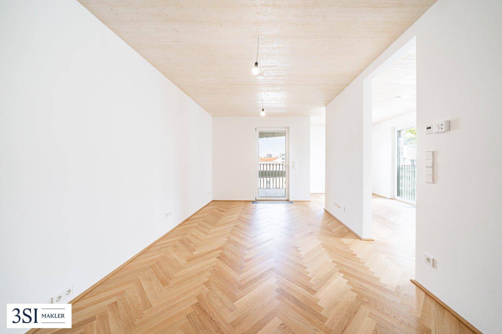 Langer, heller Wohnraum mit Fischgrätparkett und Zugang zu einem französischen Balkon.