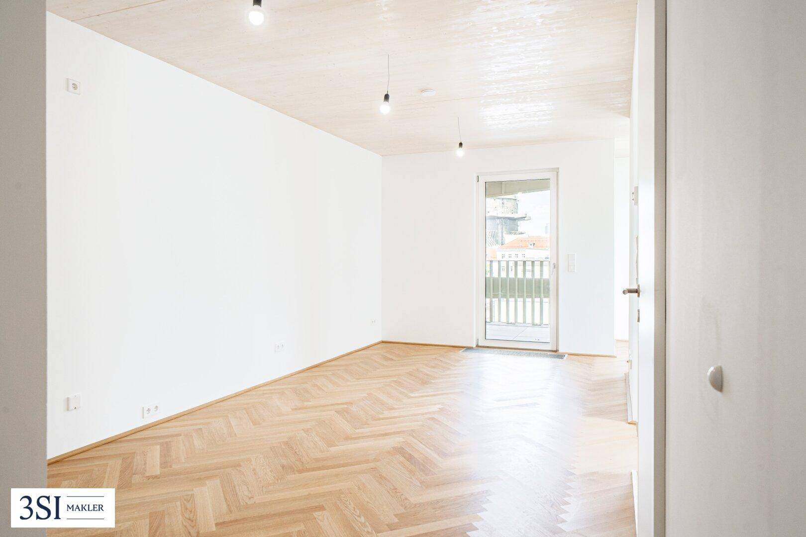 Geräumiges, helles Zimmer mit Fischgrätparkett und Zugang zu einem französischen Balkon.