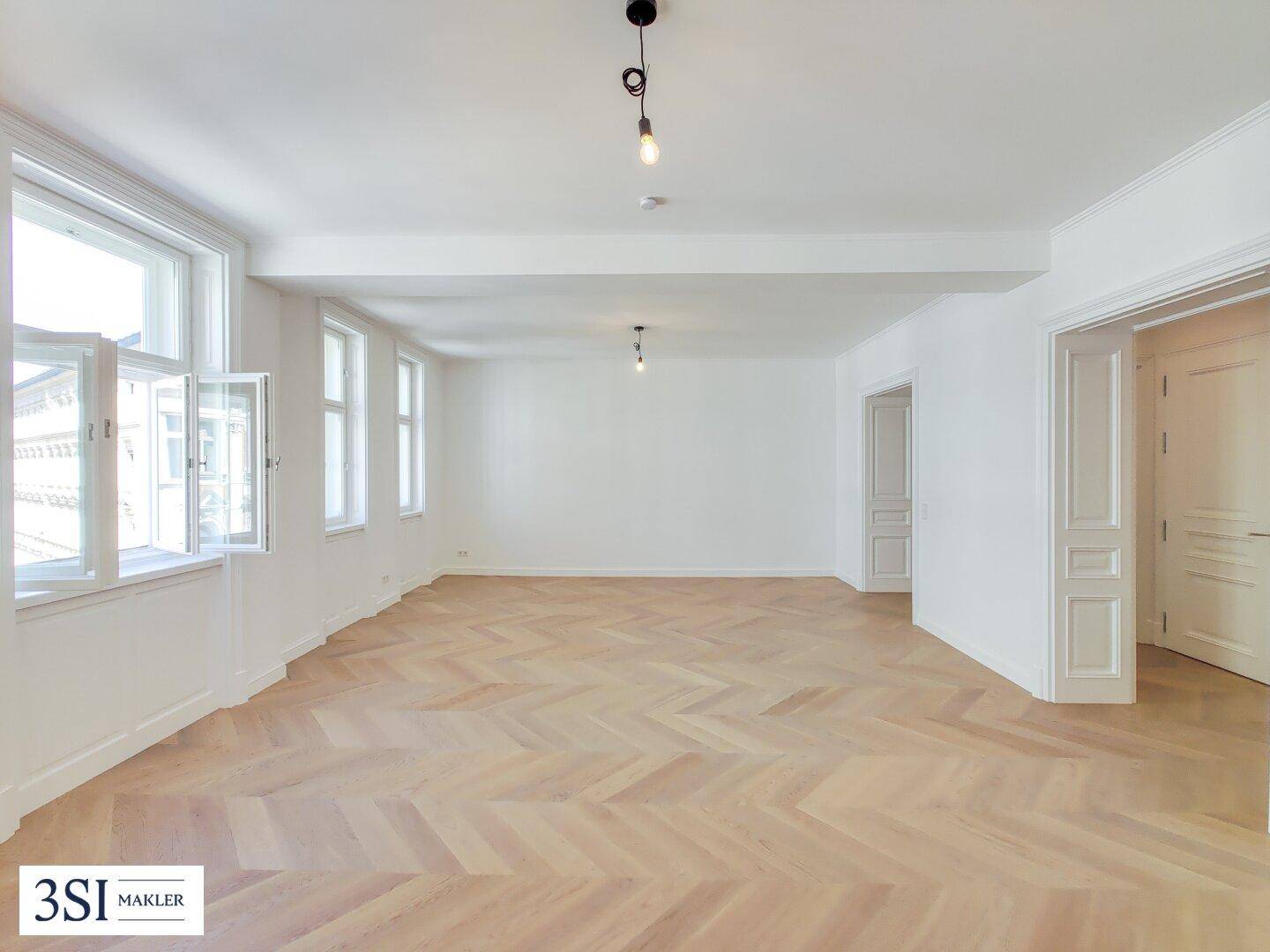 Geräumiges Wohnzimmer mit viel Tageslicht, Fischgrätparkett und mehreren Fenstern.