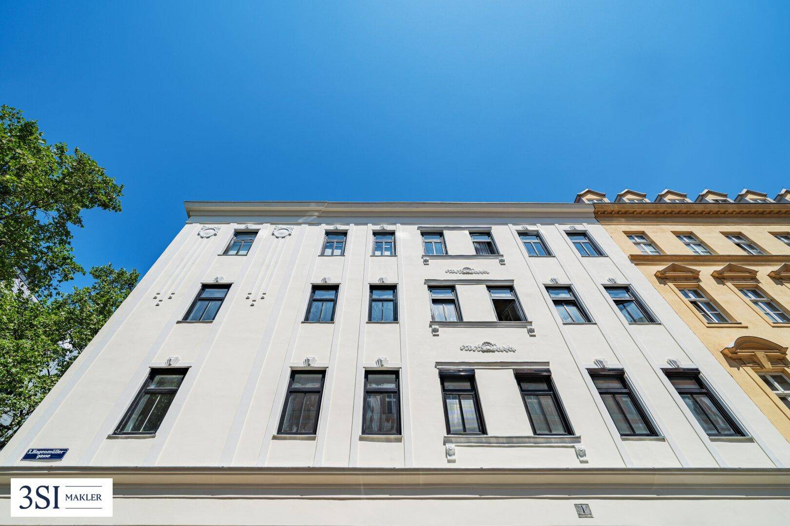 Die moderne, helle Fassade des Gebäudes mit zahlreichen Fenstern unter blauem Himmel.
