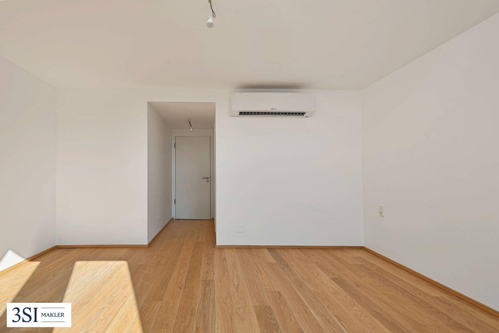 Helles, unmöbliertes Zimmer mit Holzboden und Klimaanlage.