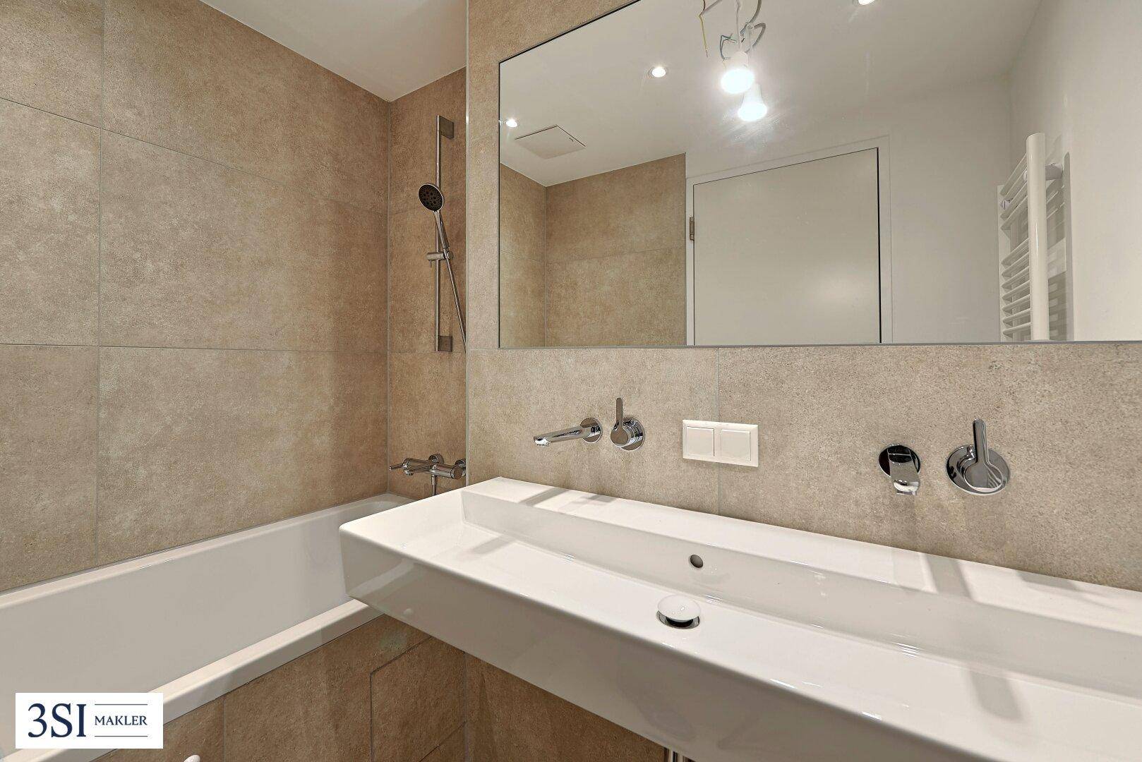 Modernes Badezimmer mit Badewanne, großem Waschbecken und beigefarbenen Fliesen.