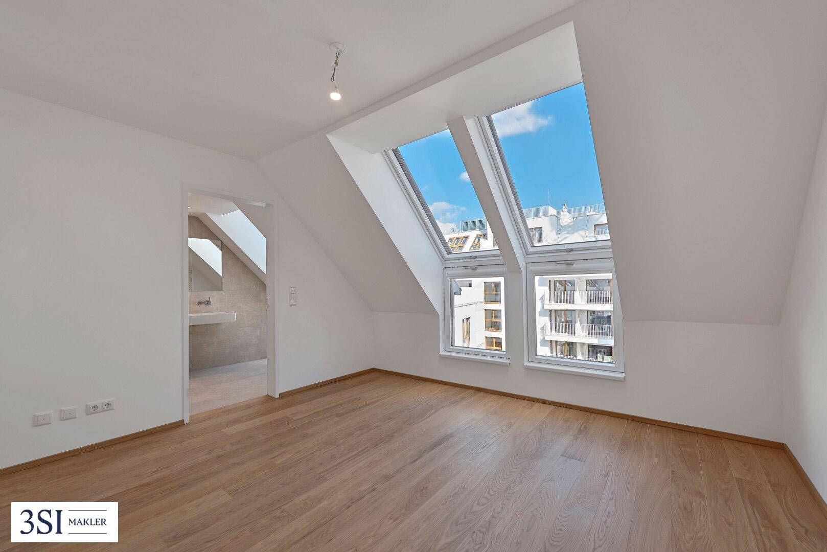 Unmöbliertes Schlafzimmer mit Holzboden, Dachfenstern und Blick auf die Stadt.