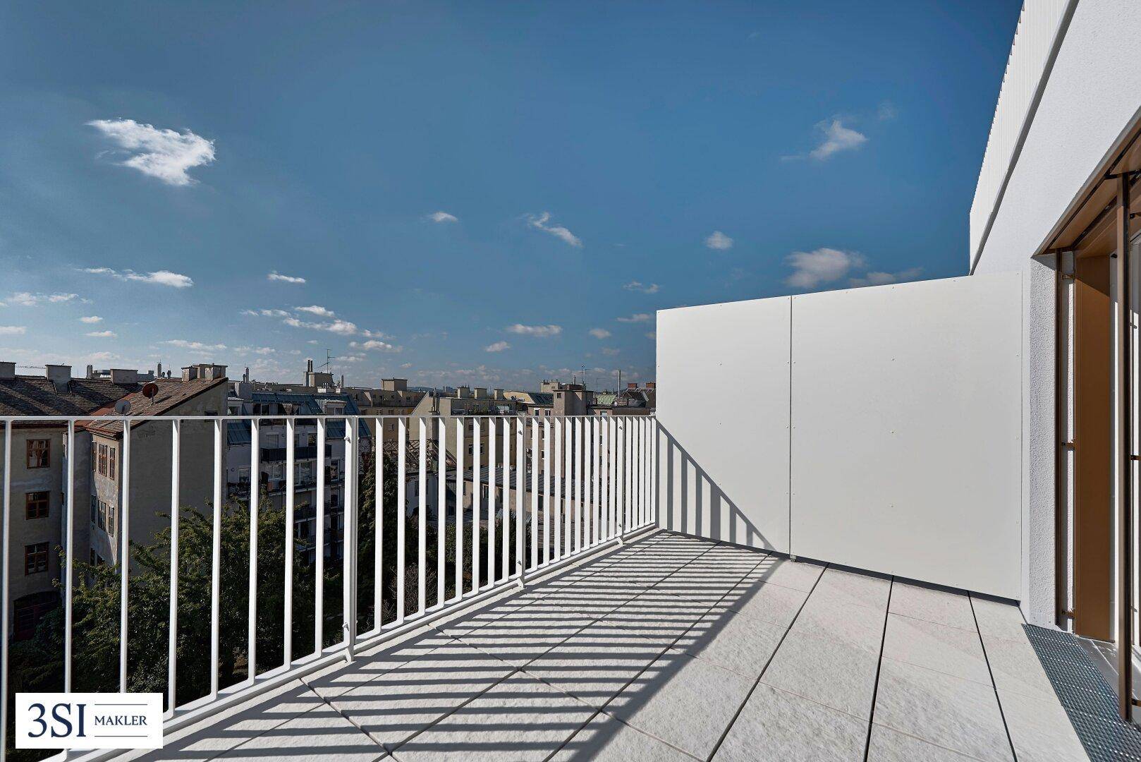 Sonniger Terrassenbereich mit weißem Geländer und Blick auf die Stadt.