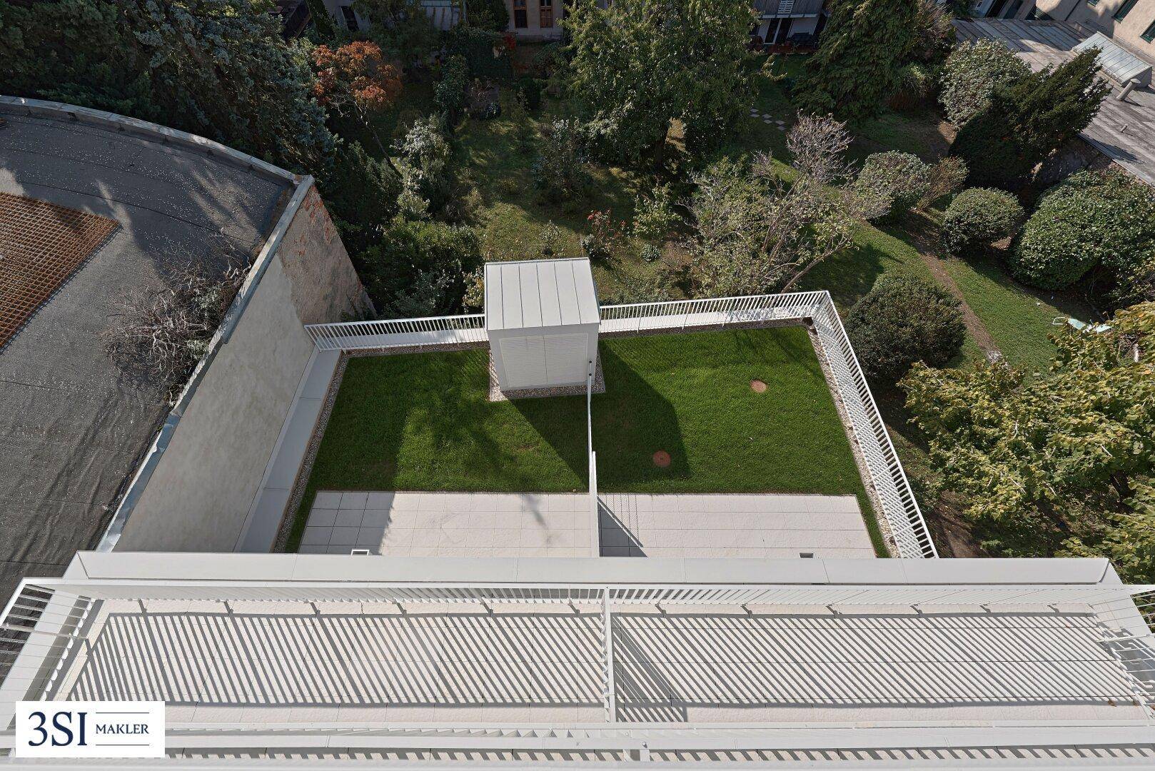 Dachterrasse mit Grünfläche und gepflastertem Bereich, umgeben von einer weißen Brüstung.