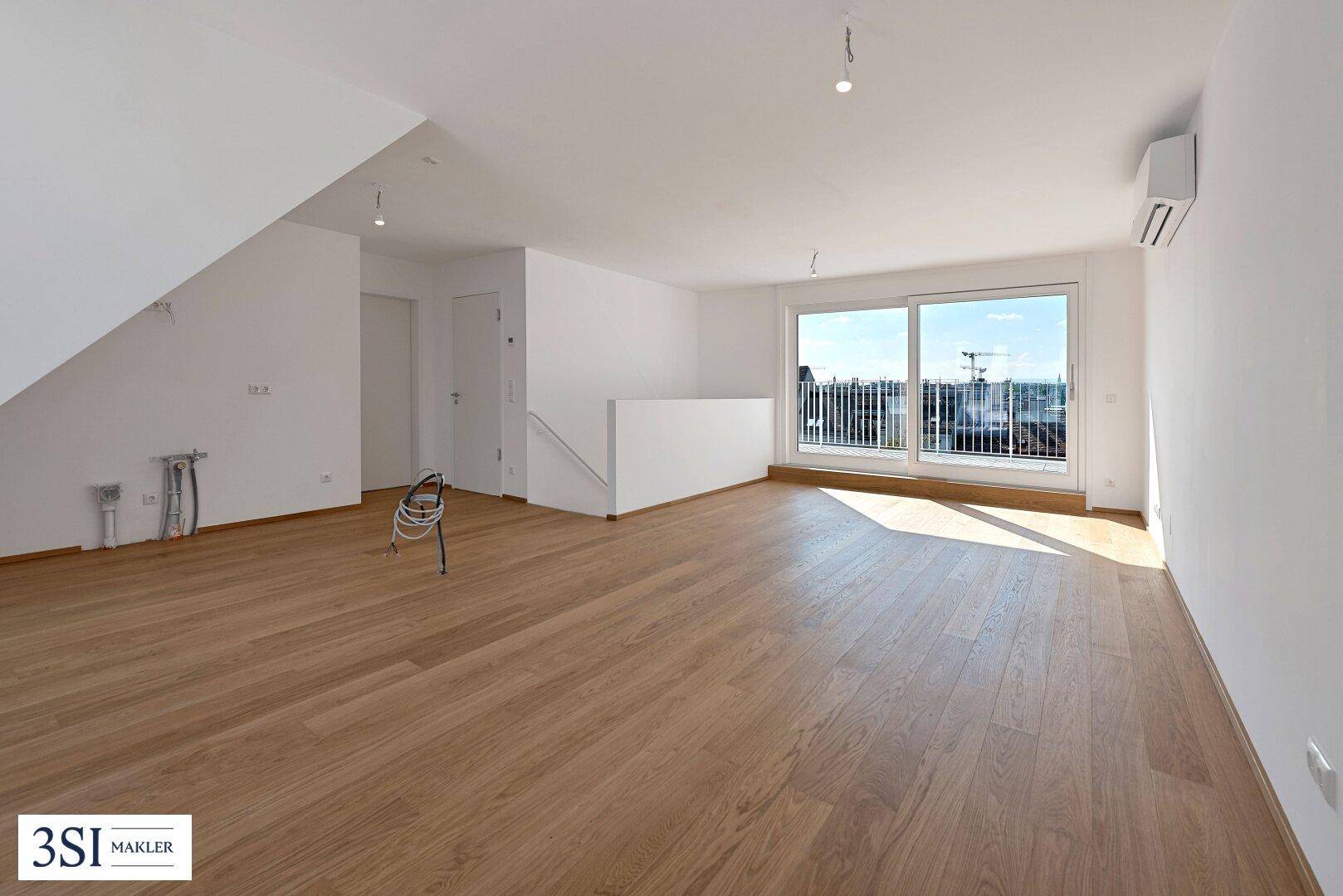 Heller, unmöblierter Wohnbereich mit Holzboden, Klimaanlage und Zugang zu einem französischen Balkon.