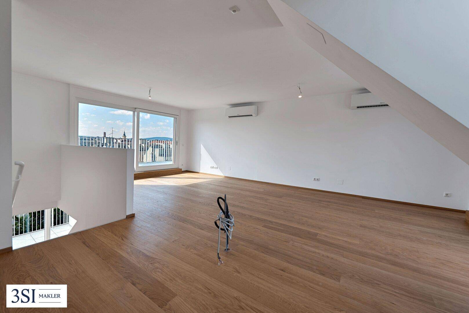 Geräumiger, heller Wohnbereich mit Holzboden, Dachschrägen und Zugang zu einem Balkon.