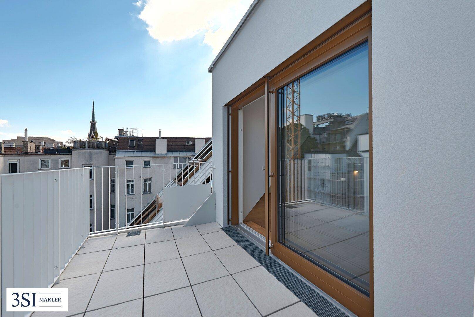 Heller Balkon mit Fliesenboden und Blick auf die Stadt, zugänglich durch eine große Glastür.