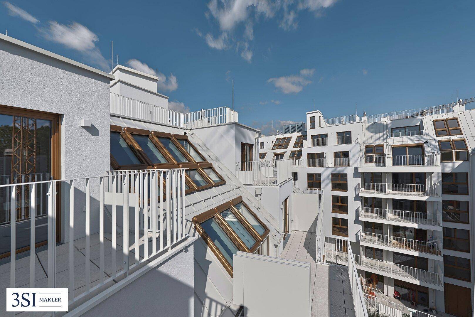 Mehrere Balkone und Dachfenster an einer modernen Gebäudefassade mit Blick auf die Stadt.