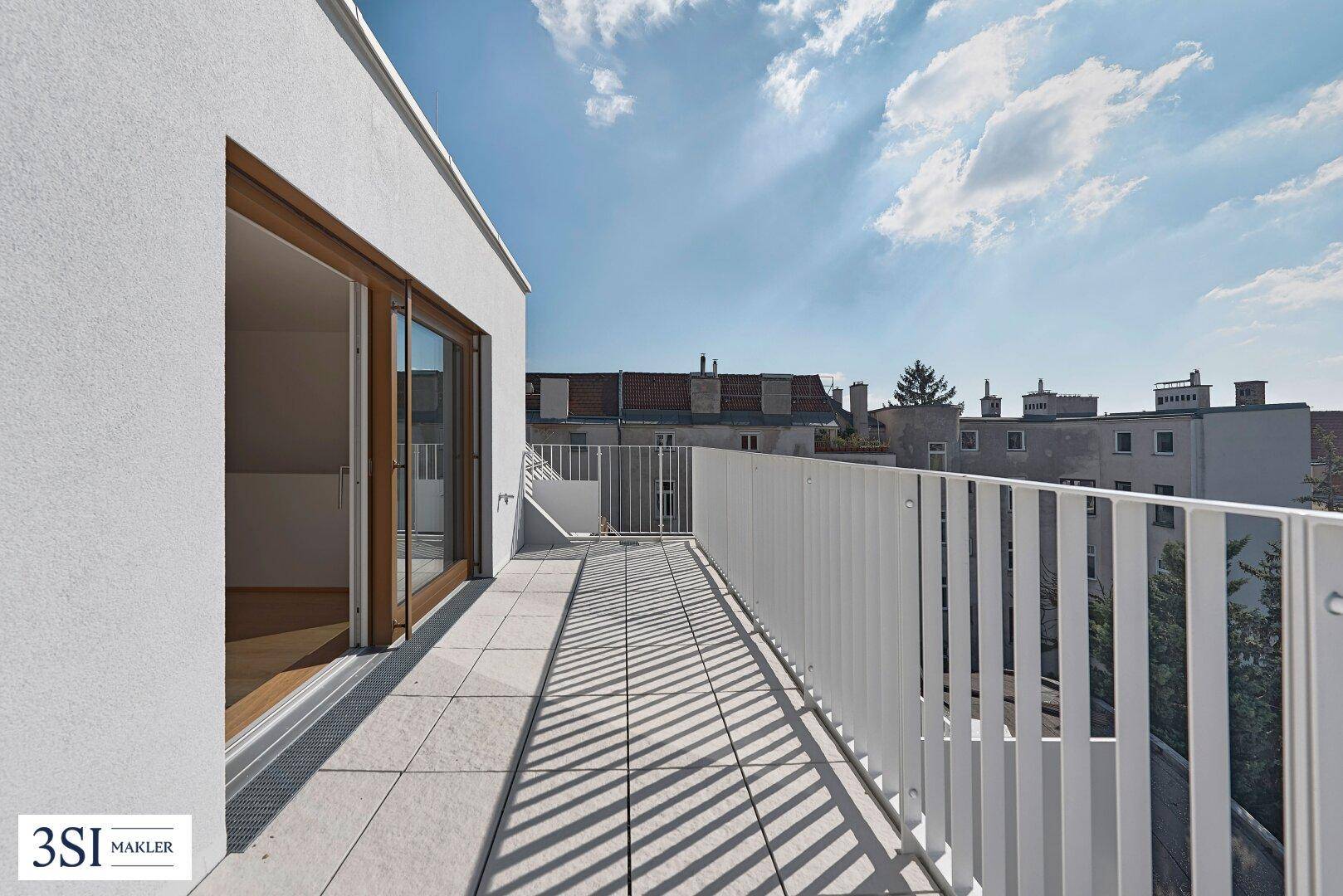 Langer, heller Balkon mit Fliesenboden und weißem Geländer, mit Zugang zum Innenraum.