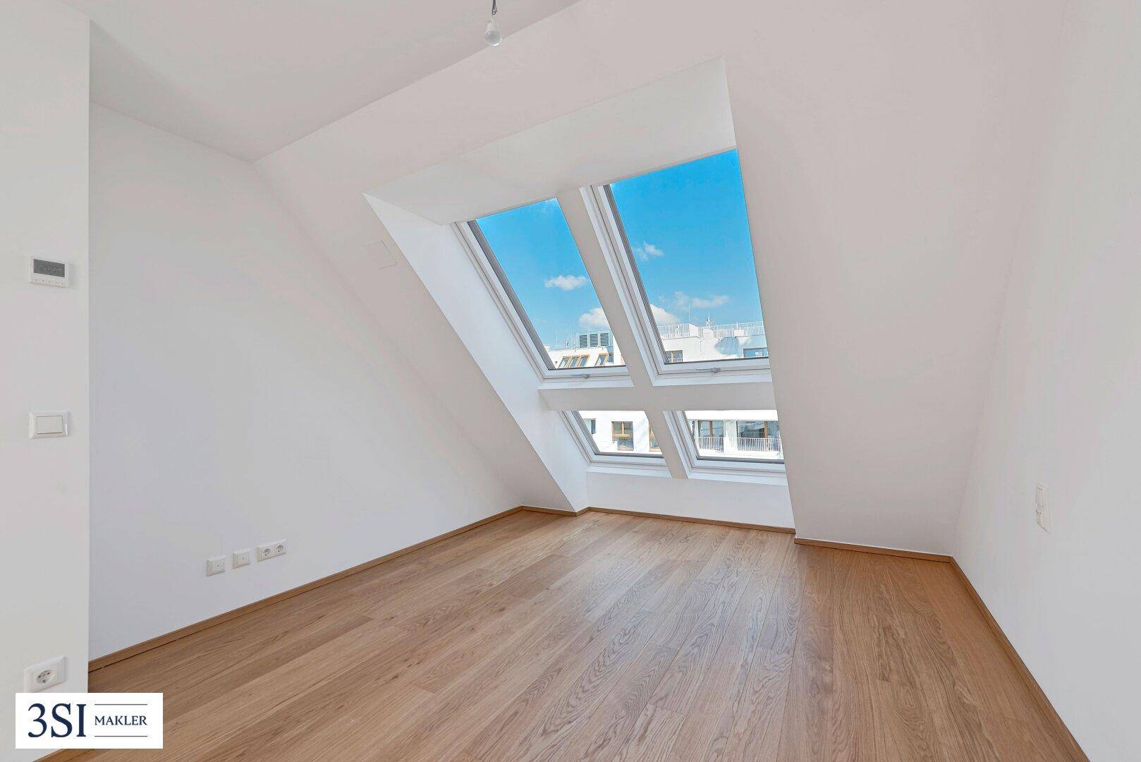 Helles Schlafzimmer mit Holzboden, Dachschrägen und großen Dachfenstern für viel Tageslicht.
