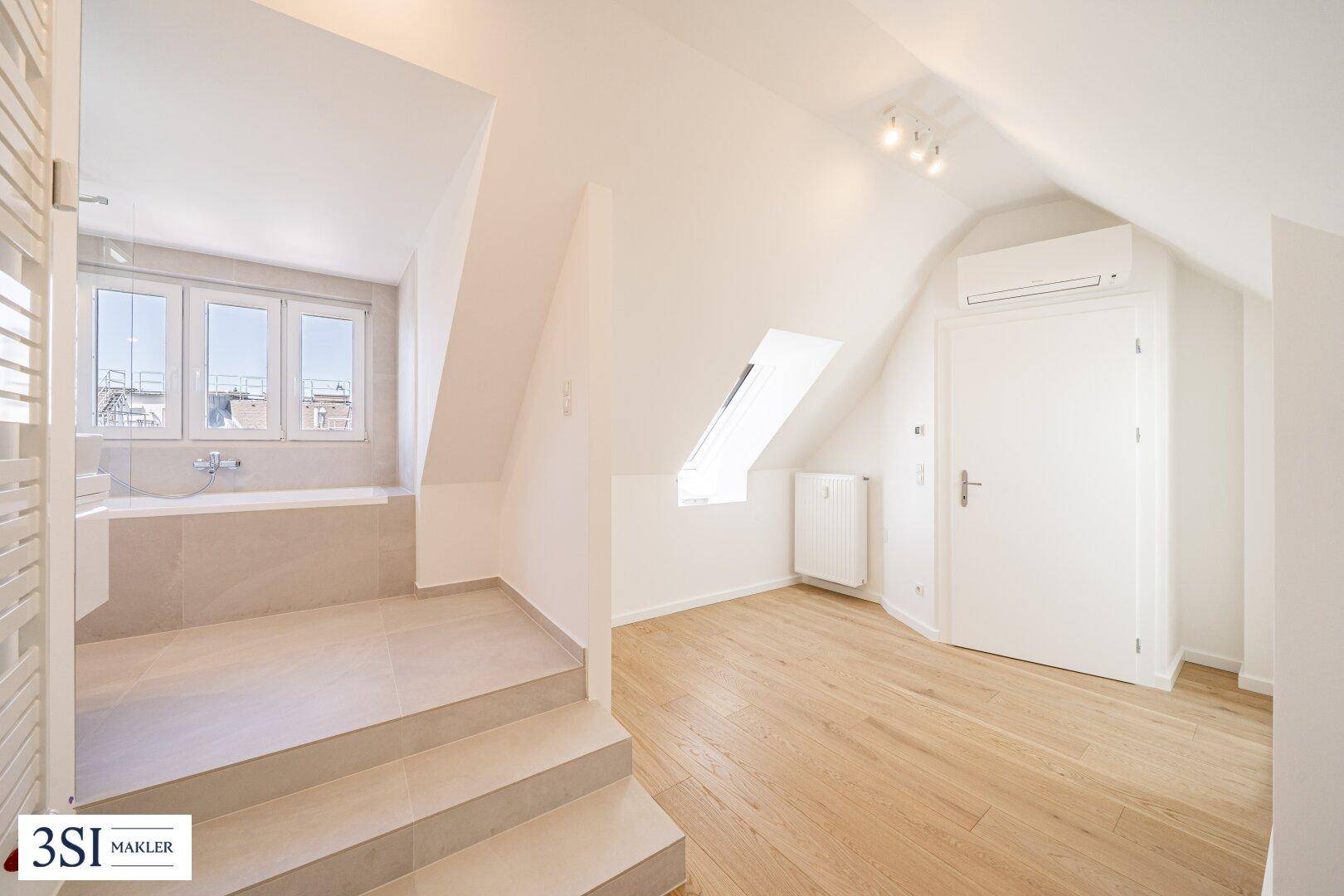 Geräumiges Dachgeschosszimmer mit Holzboden, Klimaanlage und offenem Zugang zu einem Badezimmer.