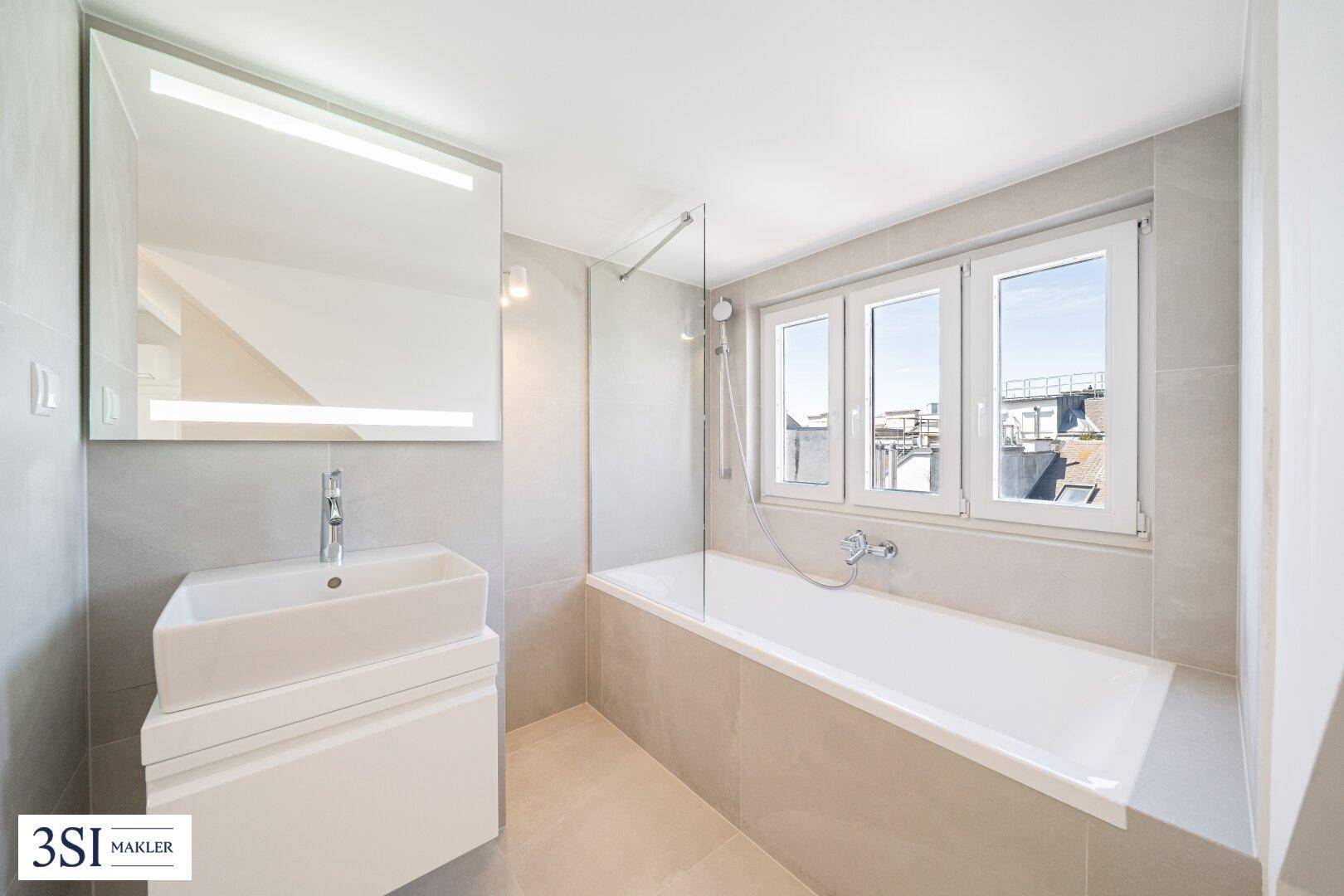 Modernes Badezimmer mit Badewanne, Einzelwaschbecken, Spiegelschrank und Fenster für Tageslicht.