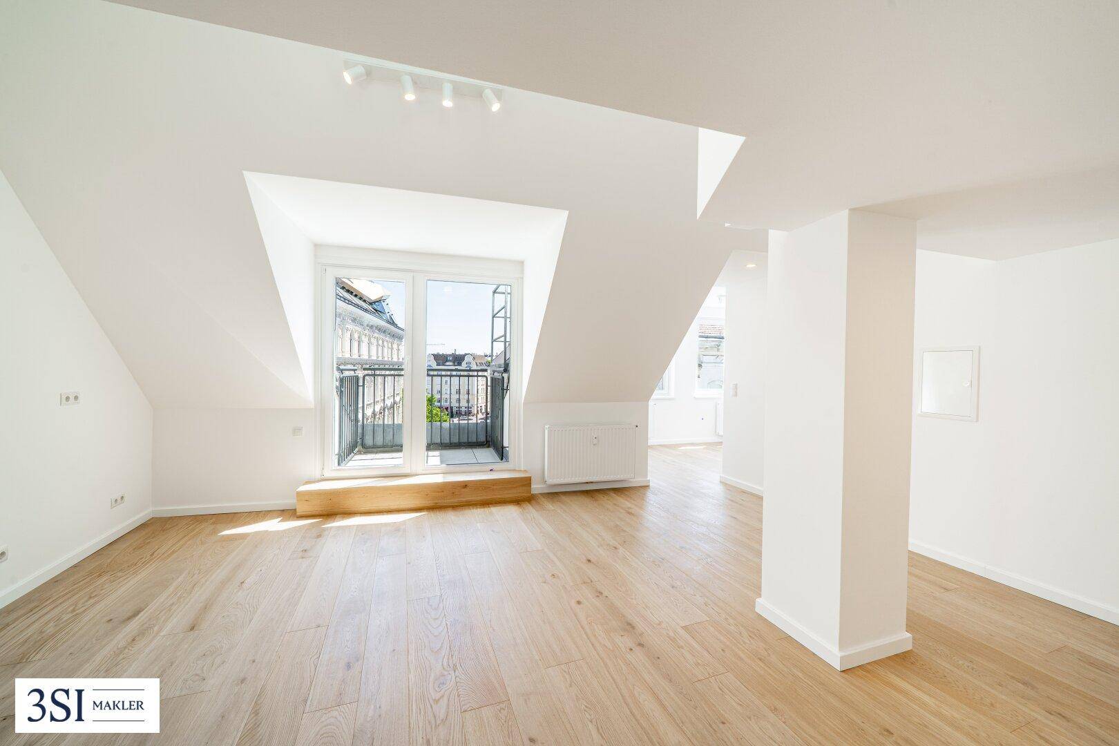 Helles Dachgeschosszimmer mit Holzboden, weißen Wänden und Zugang zu einem französischen Balkon.