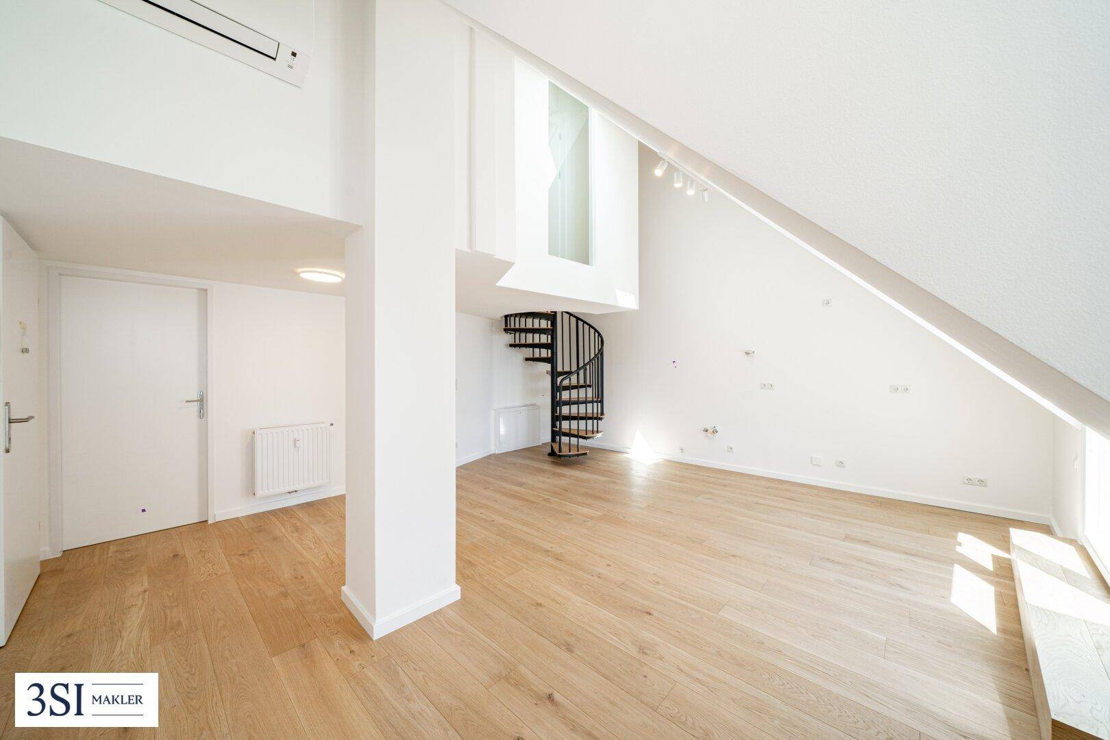 Heller Dachgeschossraum mit Holzboden, weiß gestrichenen Wänden und einer eleganten Wendeltreppe.