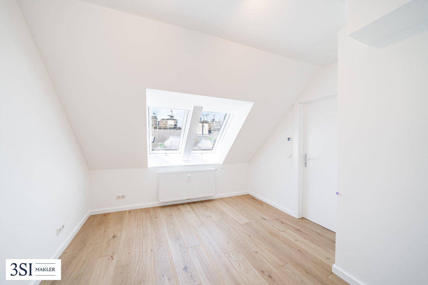 Helles Dachgeschosszimmer mit Holzboden, weißen Wänden und zwei großen Dachfenstern.
