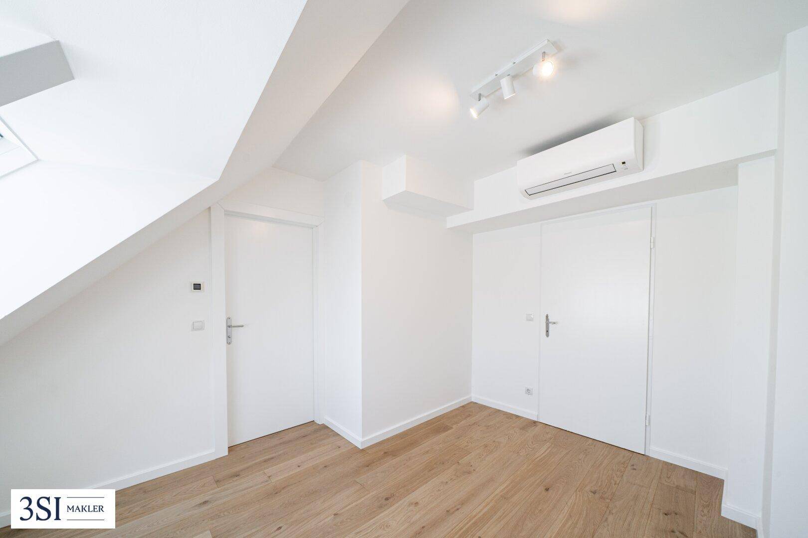 Helles Schlafzimmer mit Holzboden, Klimaanlage und praktischen Einbauschränken.