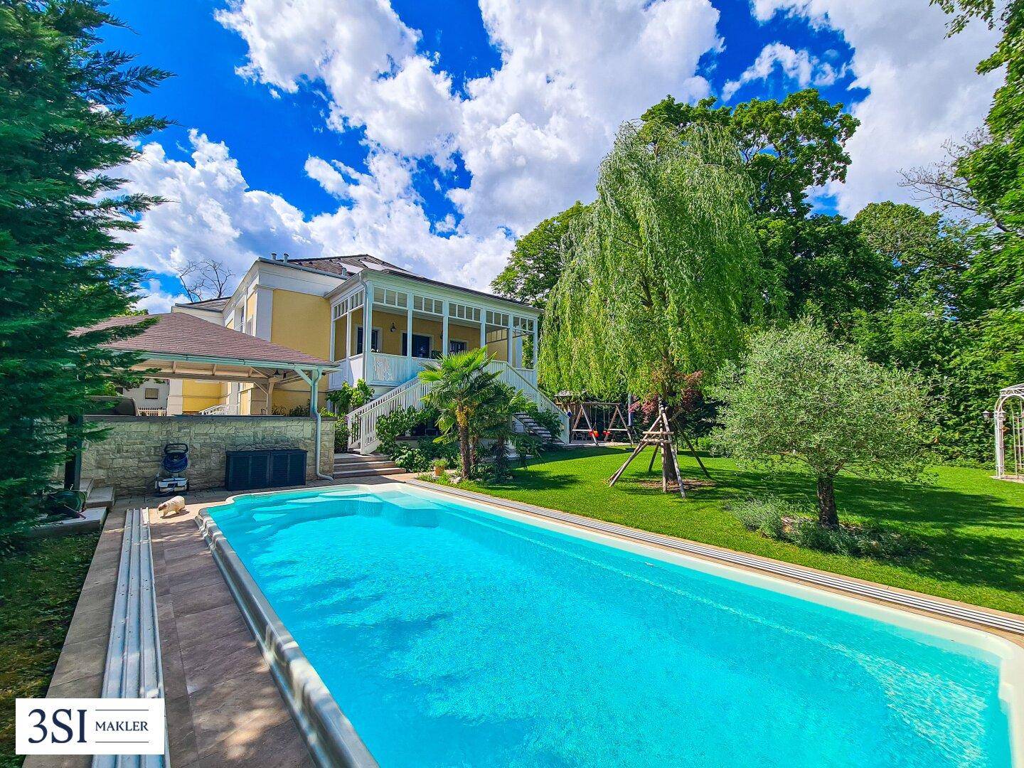 Großzügiger Garten mit erfrischendem Pool und Blick auf die elegante Villa unter blauem Himmel.