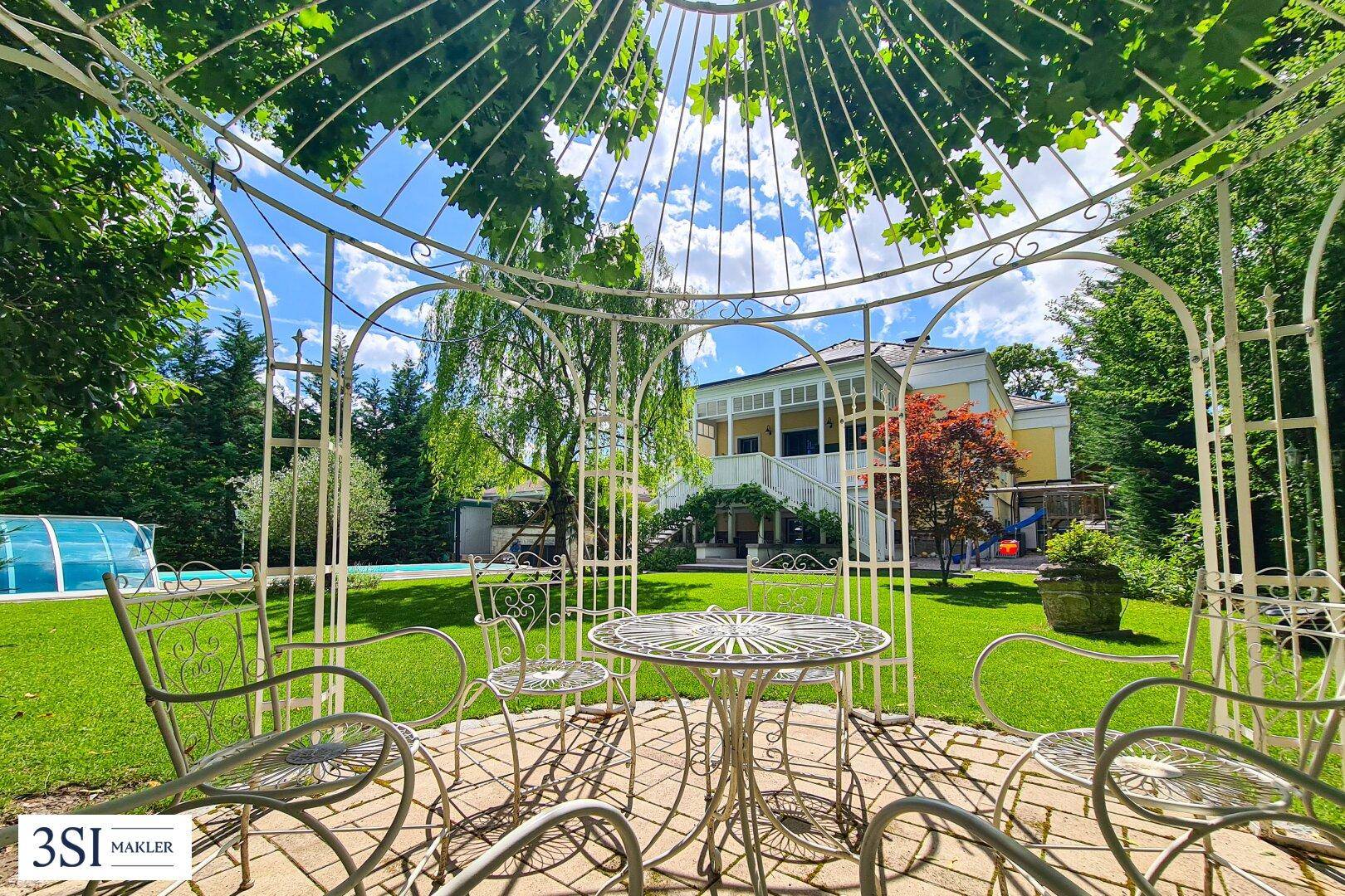 Romantischer Gartenpavillon mit Sitzgelegenheiten, bietet einen idyllischen Blick auf den Pool und das Haus.