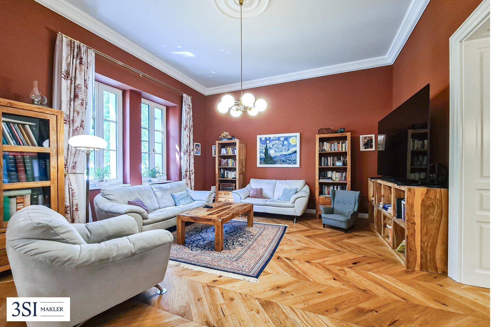 Gemütliches Wohnzimmer mit roter Wandfarbe, Fischgrätparkett und Bücherregalen, ideal zum Entspannen.