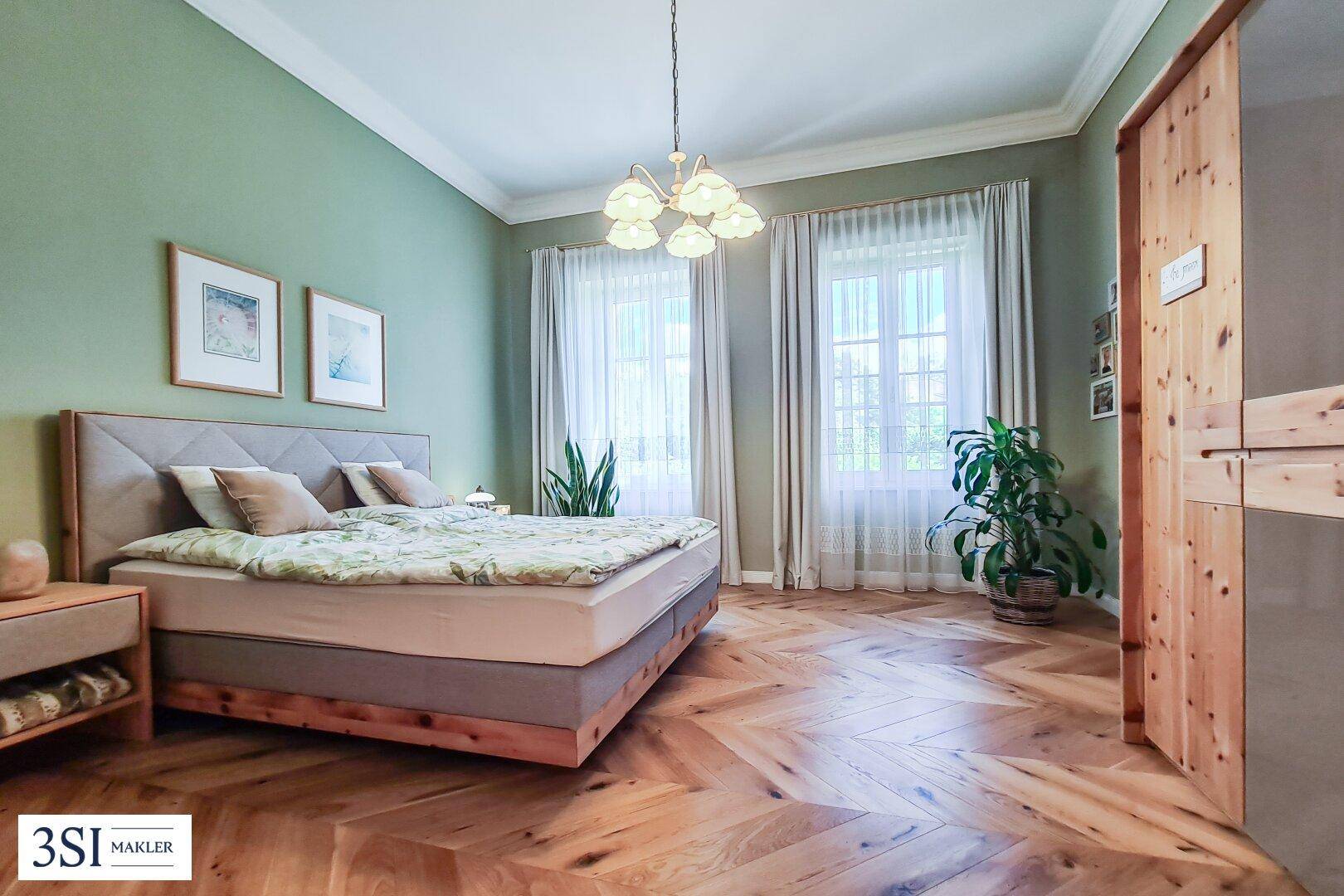 Ruhiges Schlafzimmer mit grün gestrichenen Wänden, Fischgrätparkett und großen Fenstern für viel Licht.