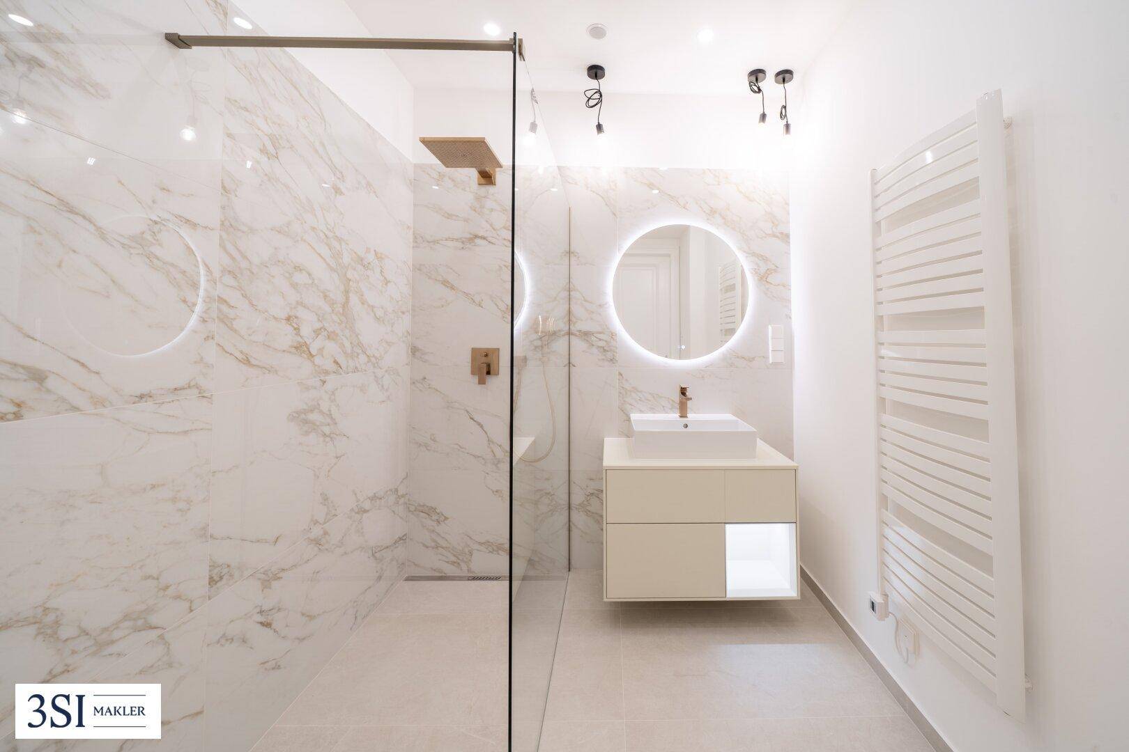 Modernes Badezimmer mit begehbarer Dusche, Marmorfliesen und beleuchtetem Spiegel.