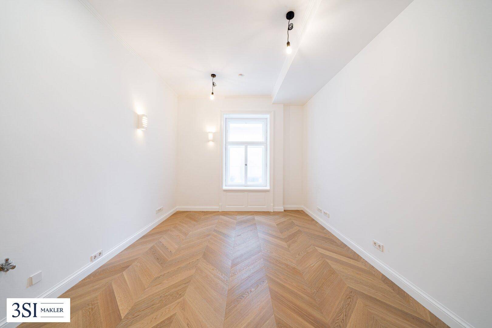 Lichtdurchflutetes Zimmer mit Fischgrätparkett, weißen Wänden und einem großen Fenster.