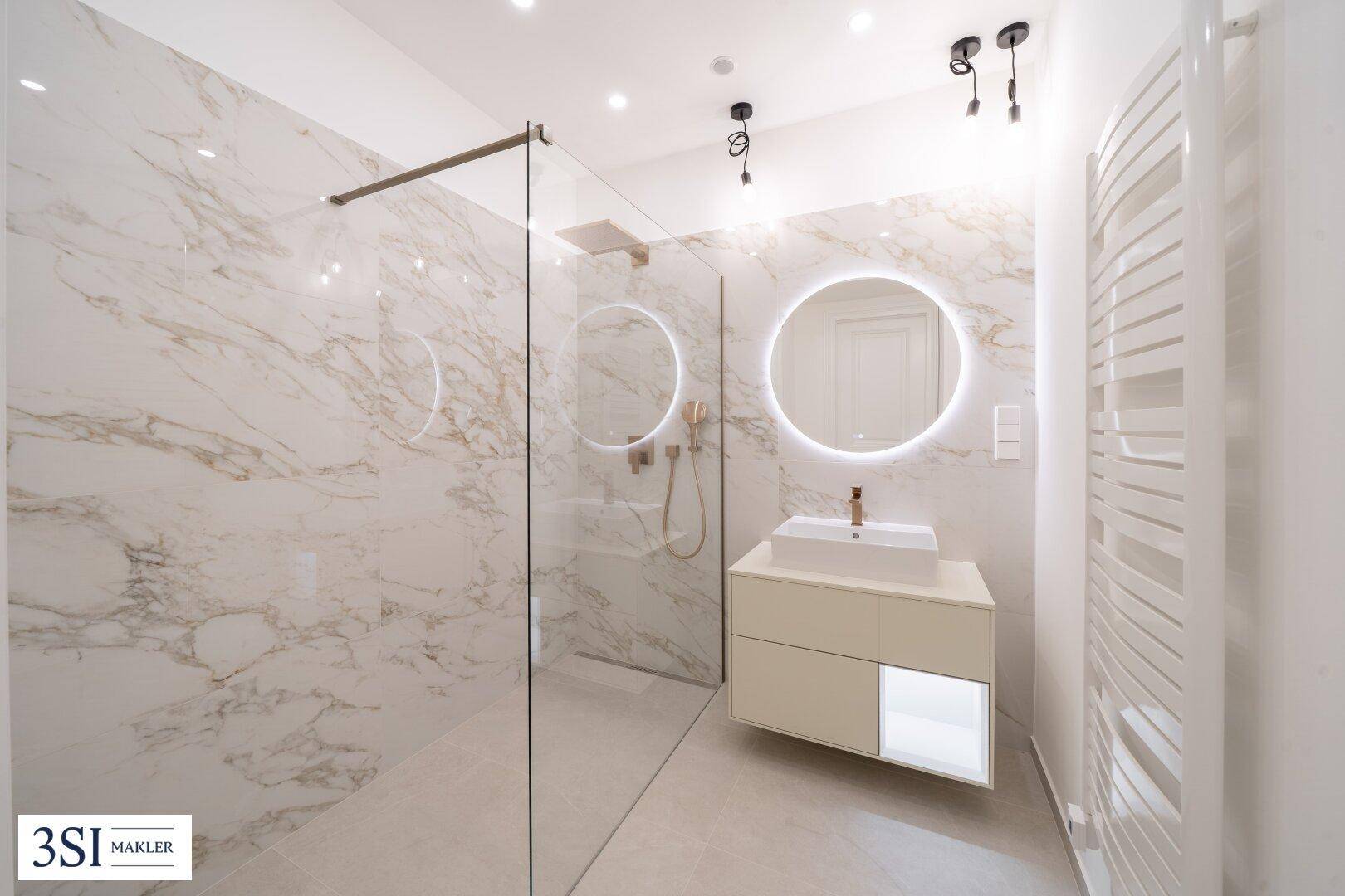 Modernes Badezimmer mit begehbarer Dusche, Marmoroptik-Fliesen und beleuchtetem Spiegel.