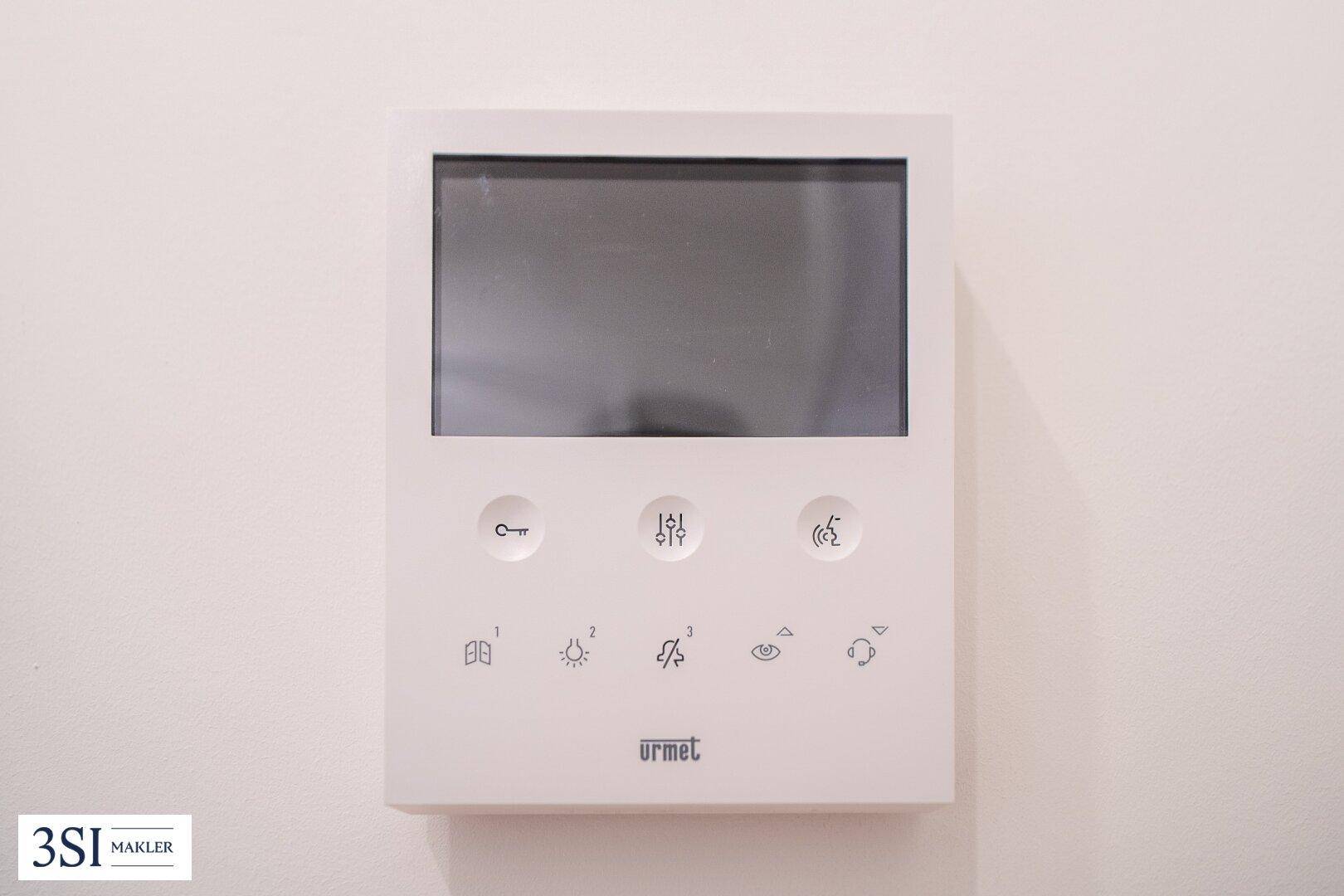 Modernes Gegensprechanlagensystem mit Bildschirm und Tasten an einer weißen Wand.
