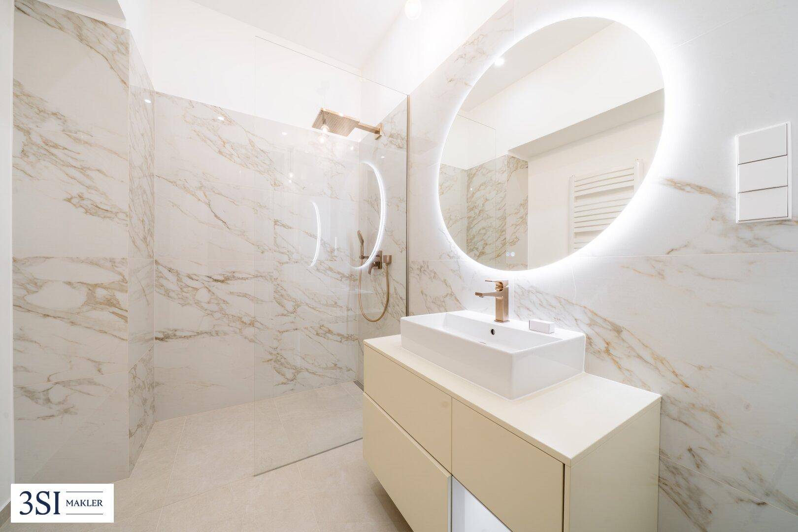 Modernes Badezimmer mit großer begehbarer Dusche, beleuchtetem Spiegel und Marmorfliesen.