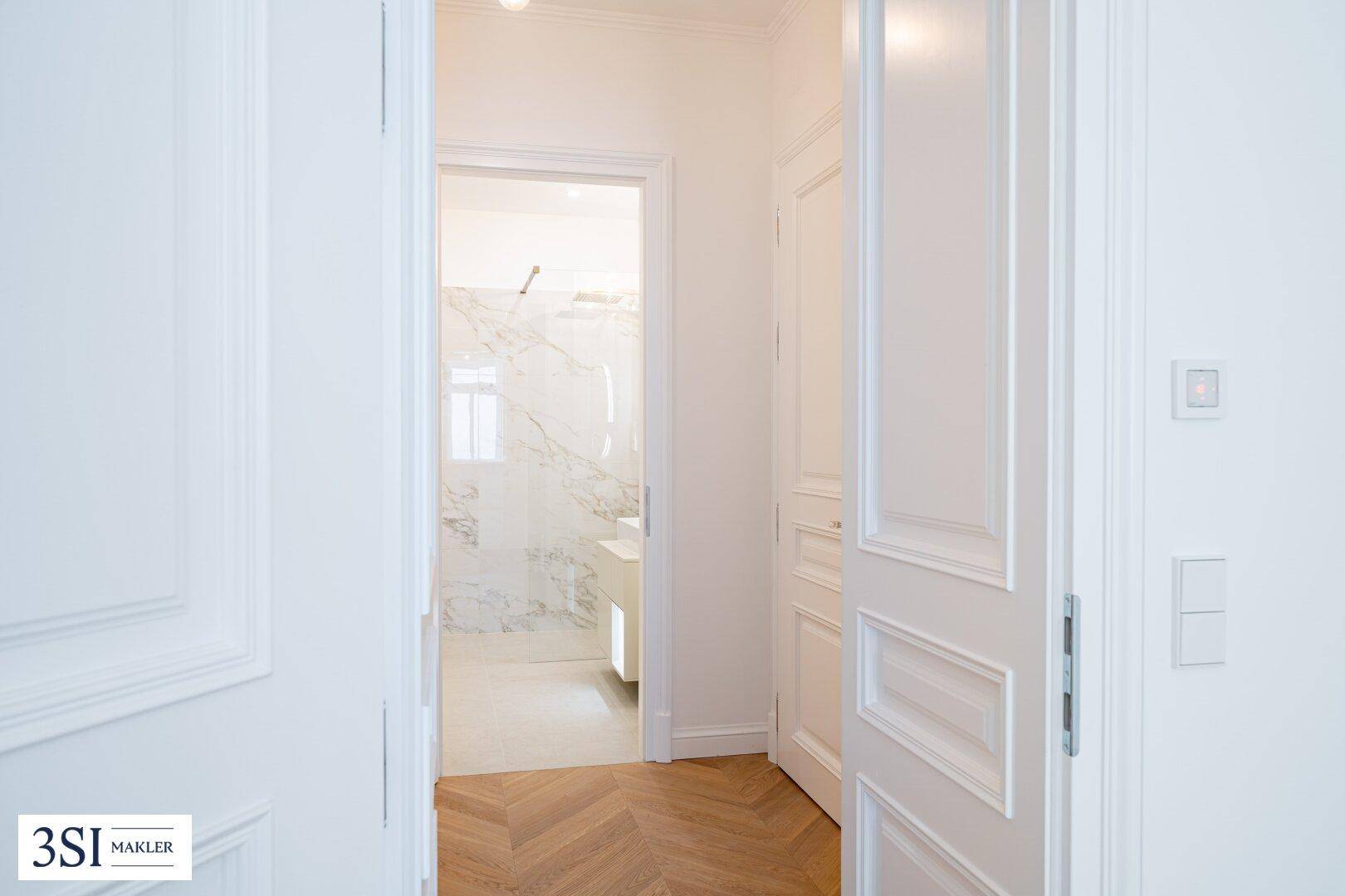 Heller Flur mit Fischgrätparkett und Blick in ein modernes Badezimmer mit Marmor.