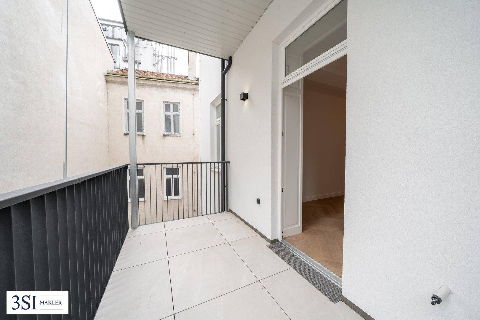 Kleiner Balkon mit Fliesenboden und Blick auf den ruhigen Innenhof des Gebäudes.