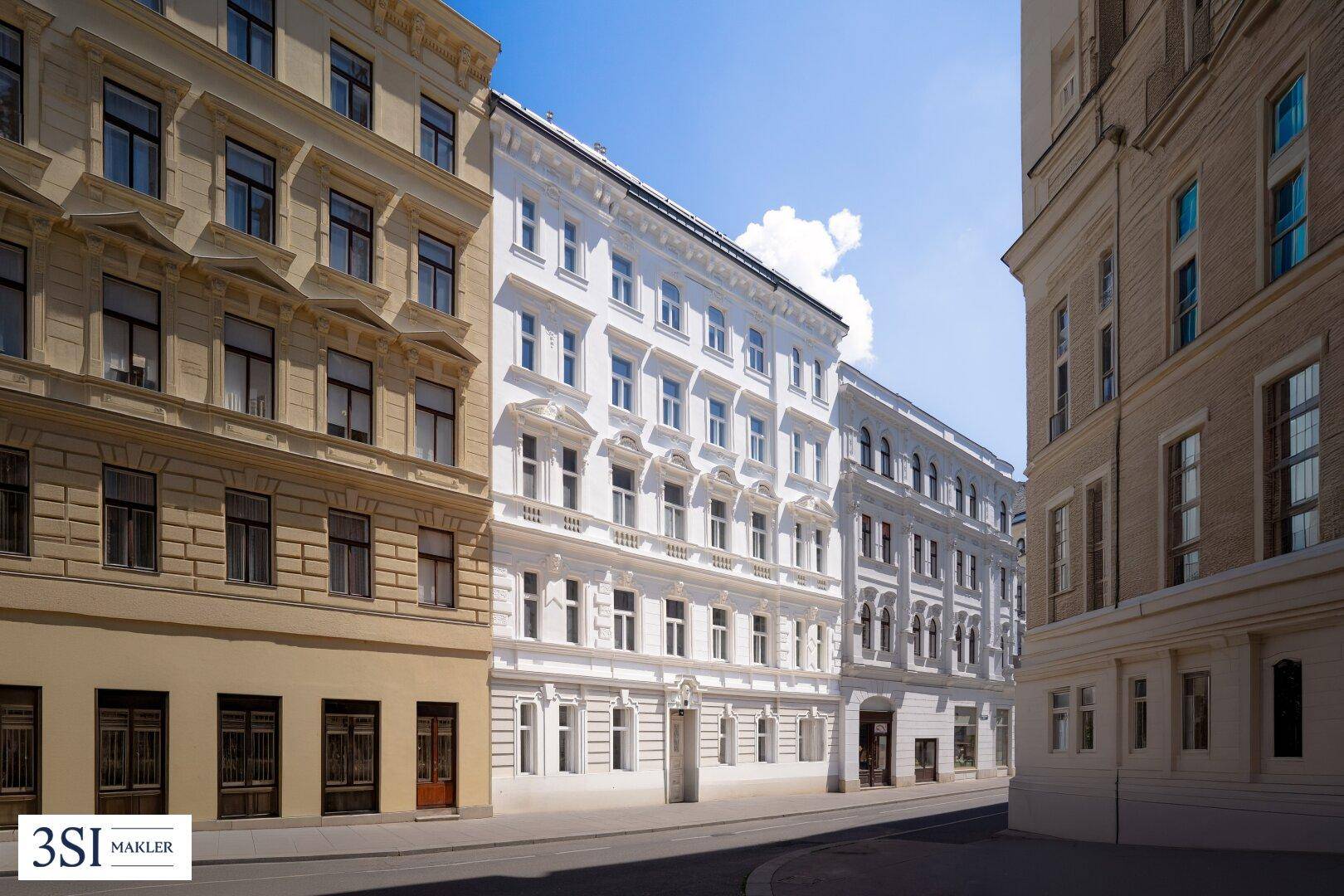 Historische Gebäudezeile in einer Stadtstraße, mit einer eleganten weißen Fassade im Vordergrund.