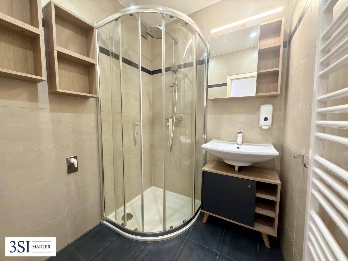 Modernes Badezimmer mit Duschkabine, Waschtisch und praktischen Ablageflächen sowie einem Handtuchheizkörper.