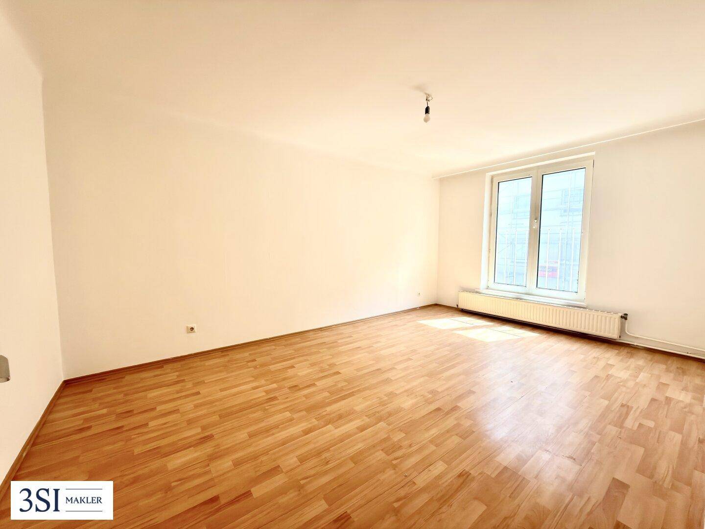 Heller, leerer Raum mit Parkettboden und großem Fenster, ideal für Wohn- oder Schlafzimmer.