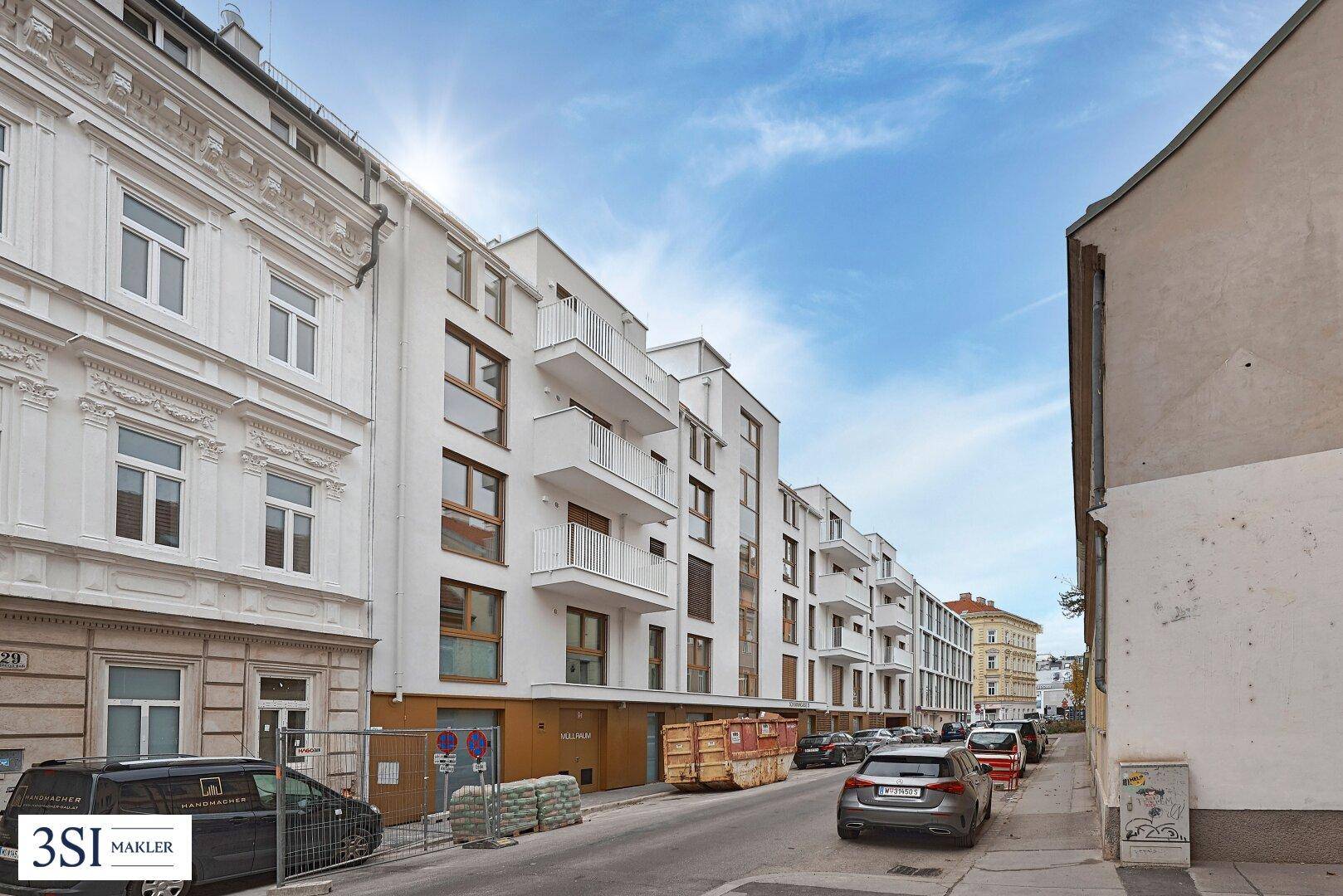 Moderne Wohngebäude mit weißen Fassaden und Balkonen an einer städtischen Straße unter blauem Himmel.