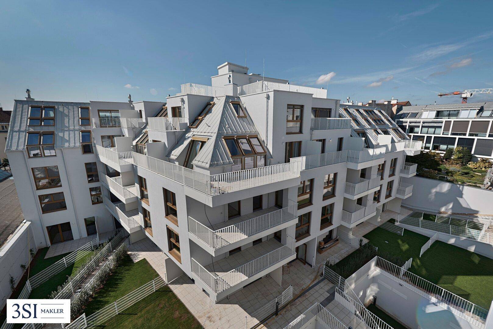 Luftaufnahme eines modernen Wohnkomplexes mit gestuften Balkonen und Dachterrassen unter blauem Himmel.