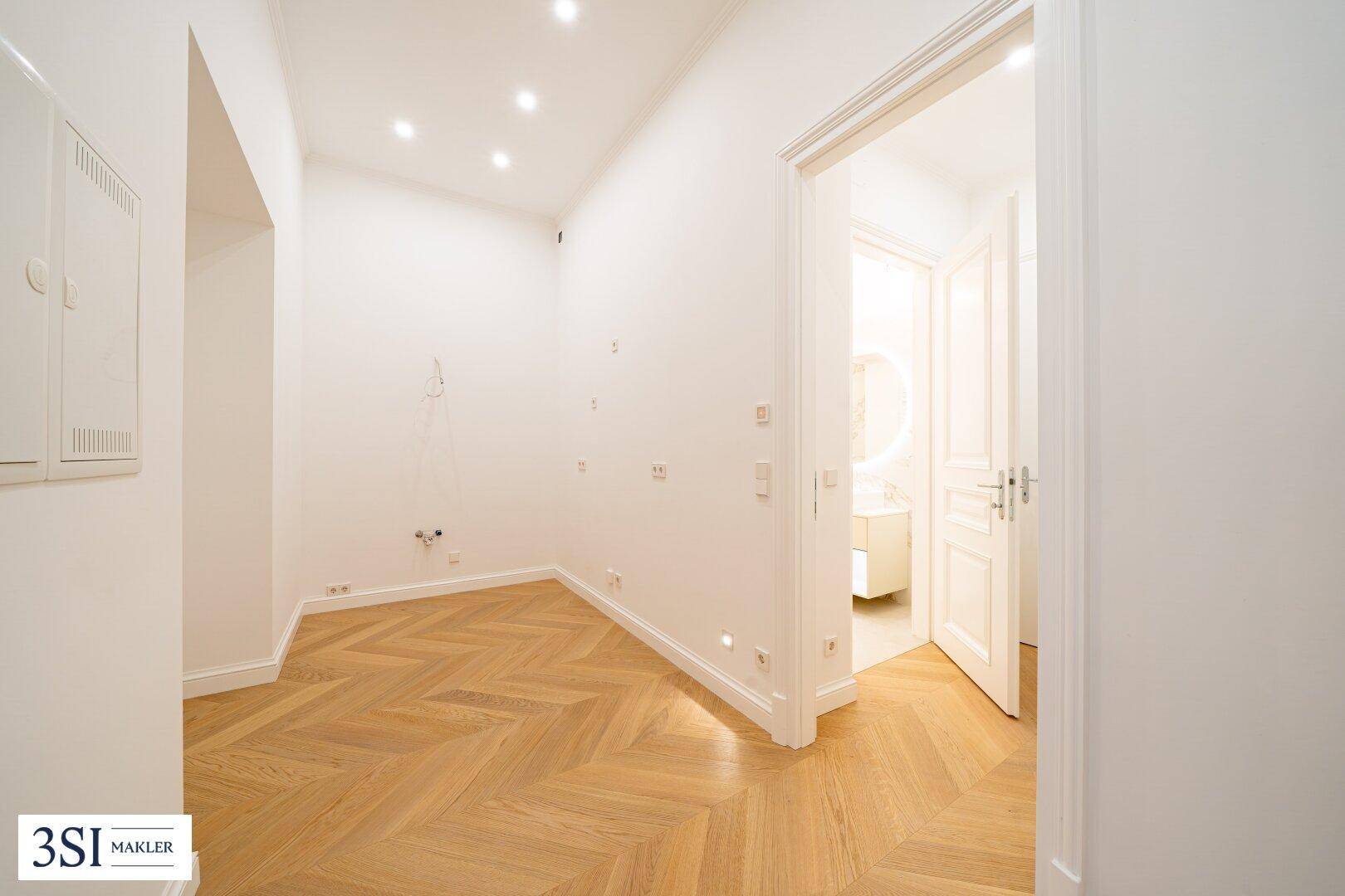 Heller Raum mit Fischgrätparkett und Zugang zu einem modernen Badezimmer.