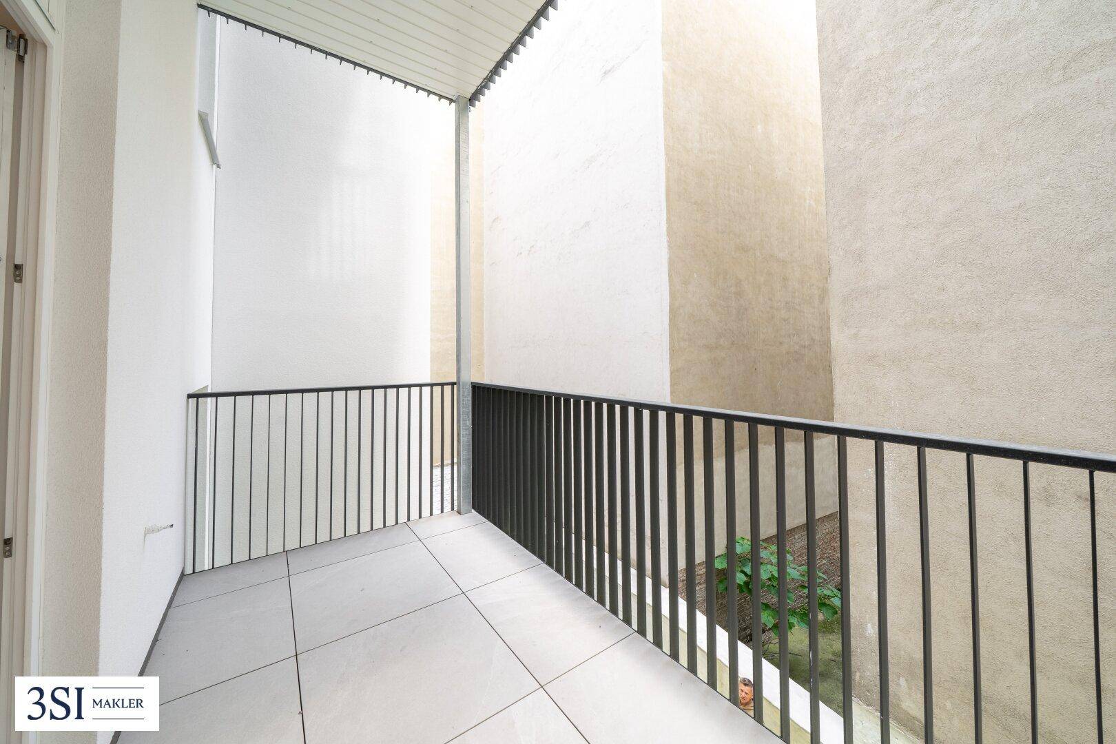 Geräumiger Balkon mit Fliesenboden und schwarzem Geländer, bietet Platz für individuelle Gestaltung.