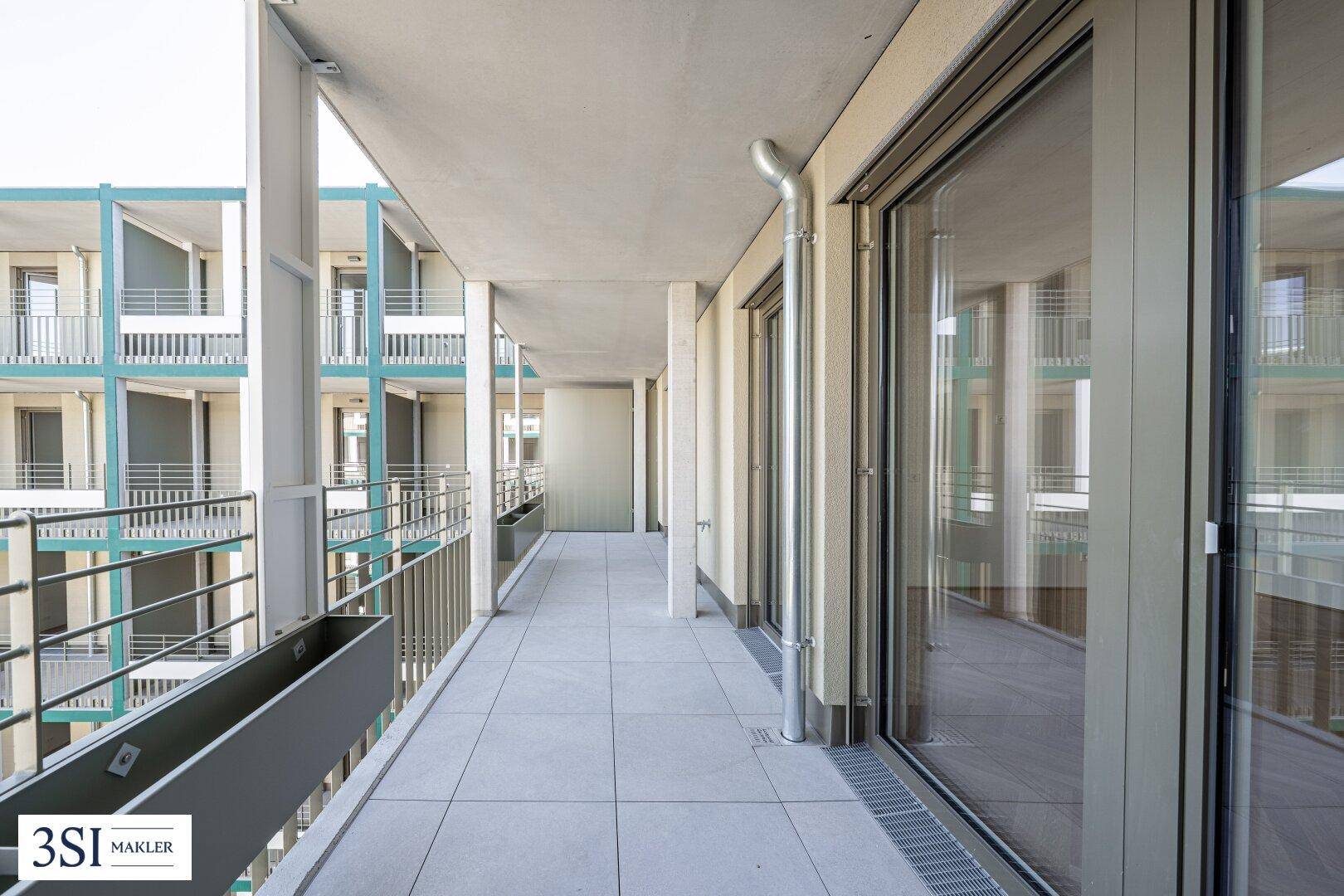Geräumiger Balkon mit Fliesenboden und großen Glasfronten, die viel Licht hereinlassen.