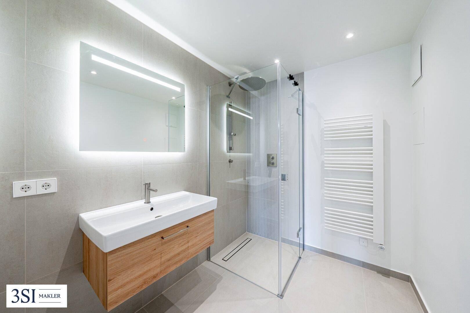 Modernes Badezimmer mit begehbarer Dusche, schwebendem Waschtisch und beleuchtetem Spiegel.