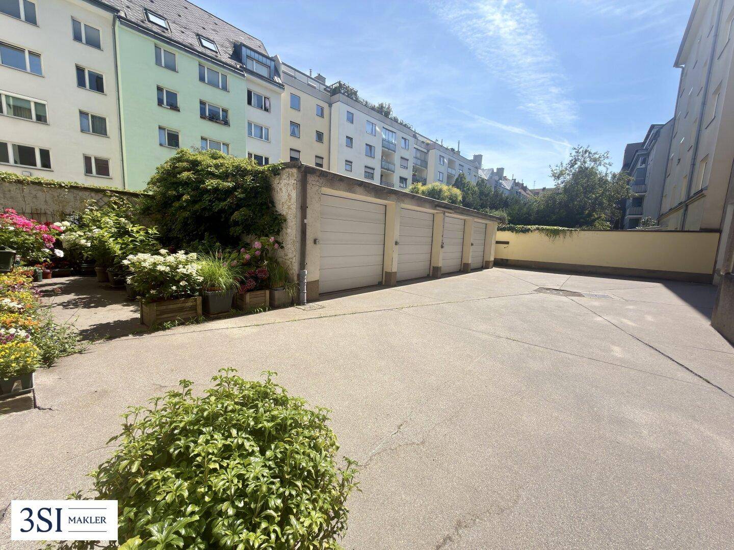 Sonniger Innenhof mit Garagenreihe und gepflastertem Parkplatz, umgeben von Wohngebäuden.