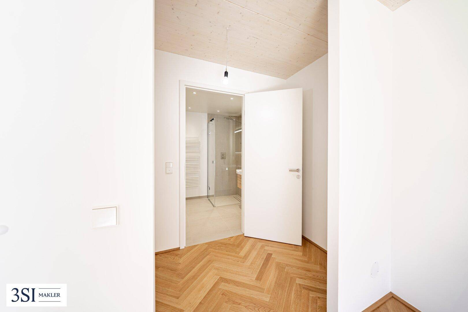 Blick von einem hellen Flur in ein modernes Badezimmer mit begehbarer Dusche.