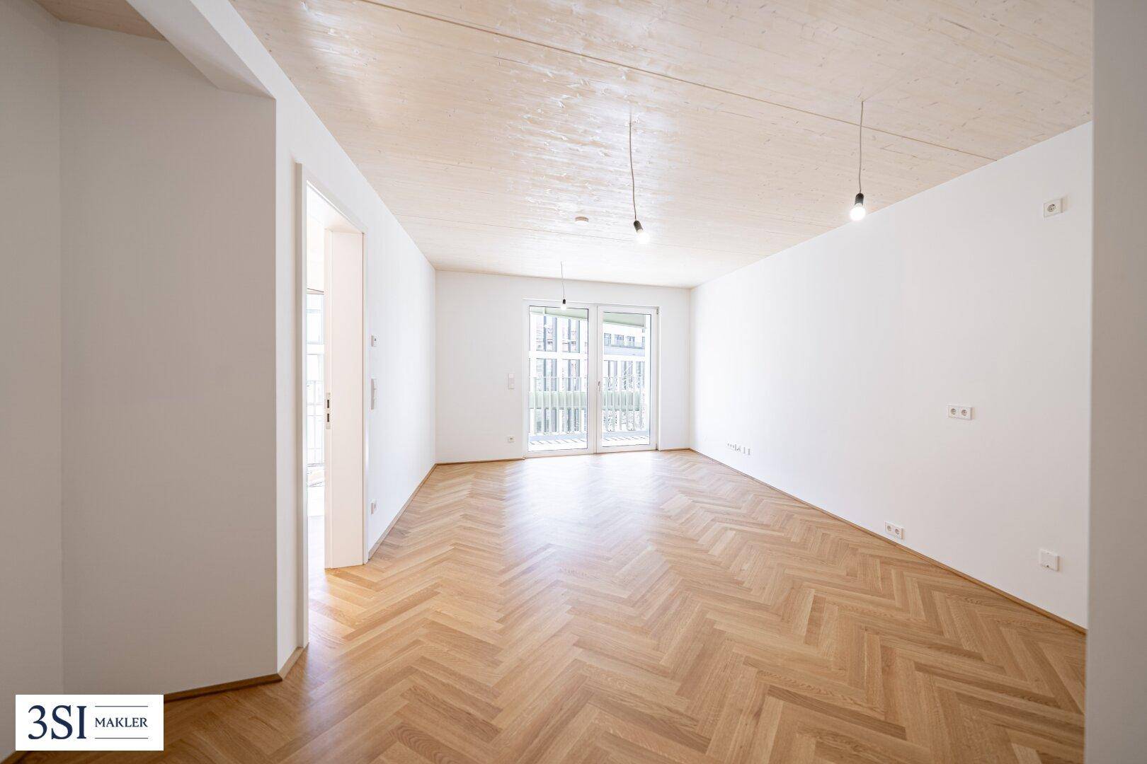 Geräumiges, leeres Wohnzimmer mit Fischgrätparkett und Zugang zu einem Balkon oder einer Terrasse.