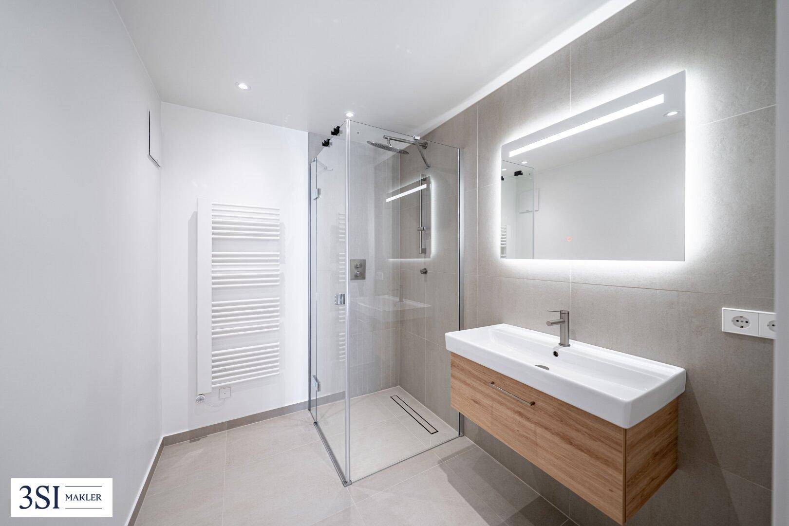 Modernes Badezimmer mit begehbarer Dusche, Wandwaschbecken und beleuchtetem Spiegel.