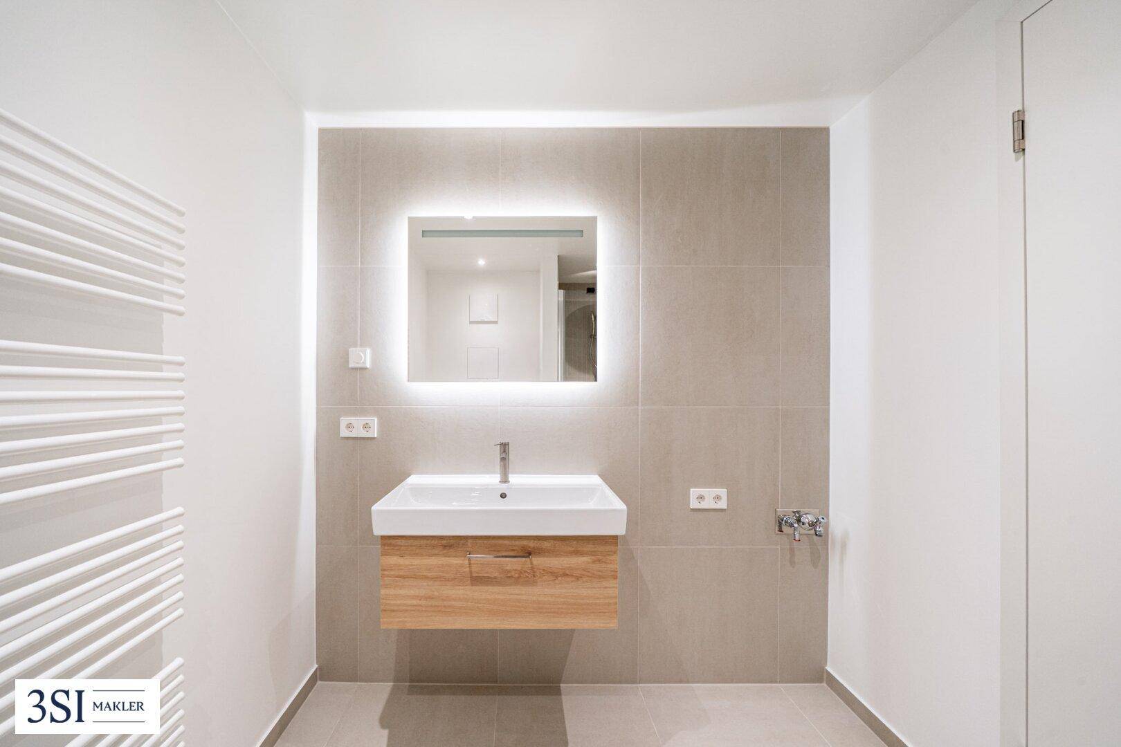 Modernes Badezimmer mit schwebendem Waschtisch, beleuchtetem Spiegel und Handtuchheizkörper.